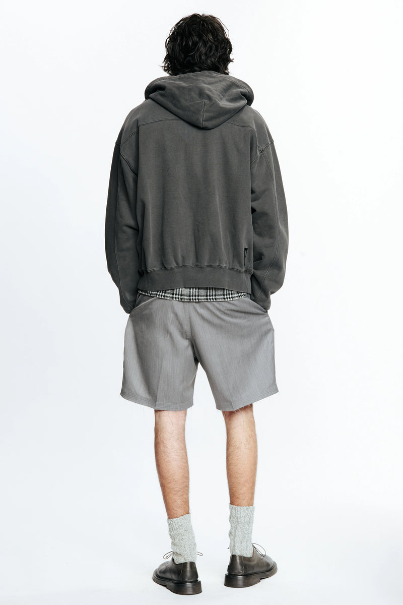 View from behind of a person wearing a grey hoodie and cut shorts on a white background