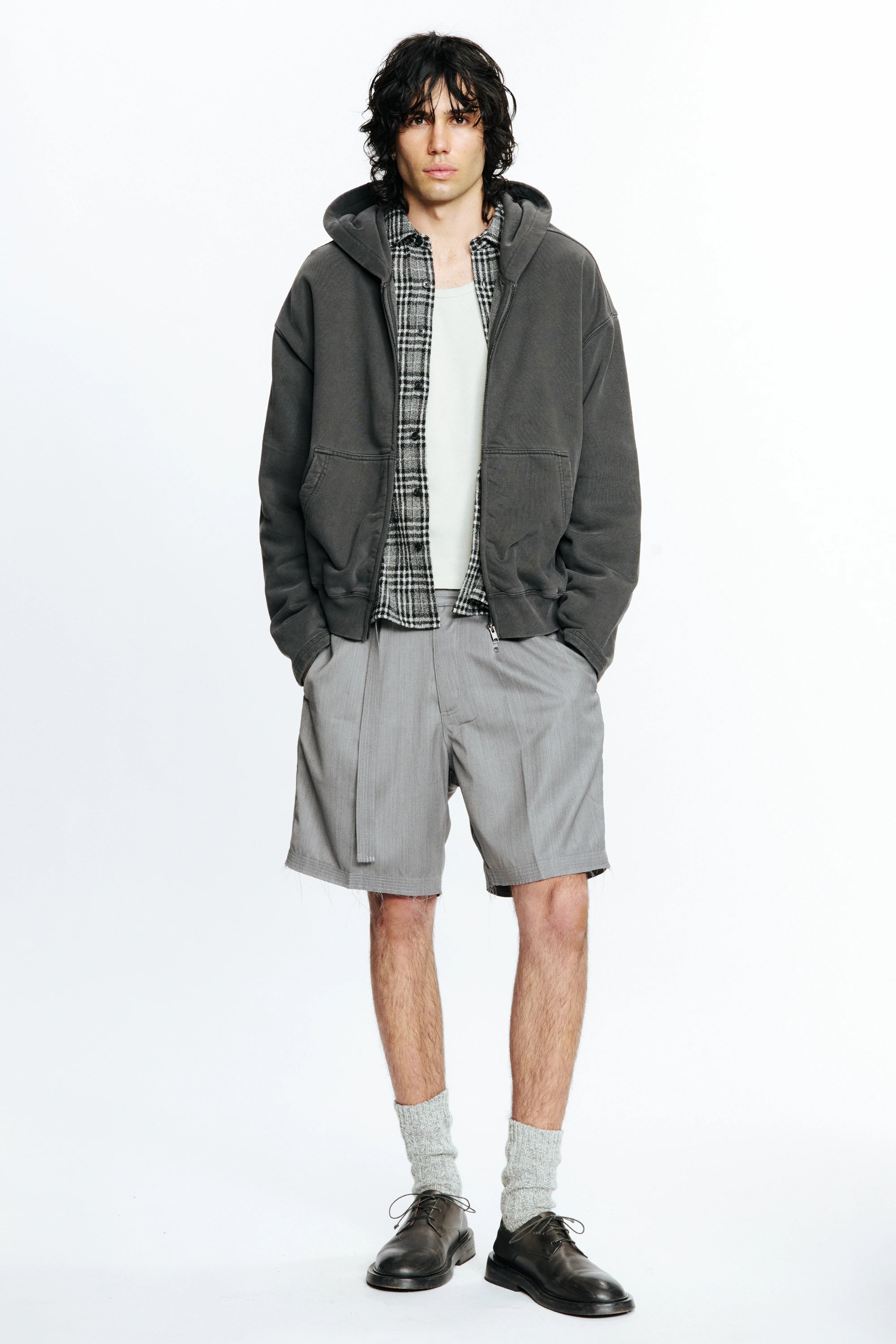 Person wearing a grey jacket, plaid shirt and grey shorts on a white background