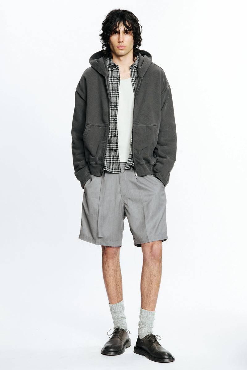 Person wearing a grey jacket, plaid shirt and grey shorts on a white background