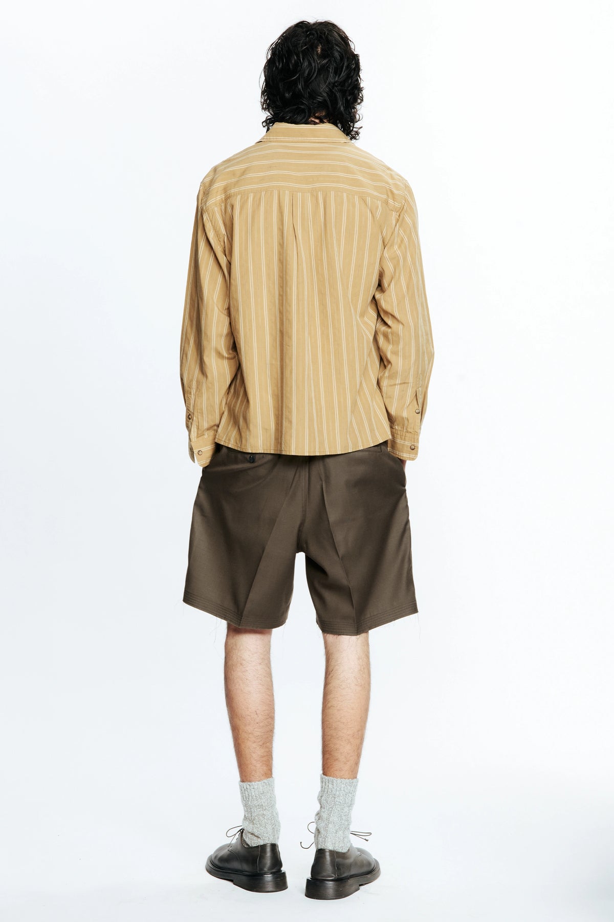 Rear view of a person wearing a beige striped shirt and brown cut shorts on a white background