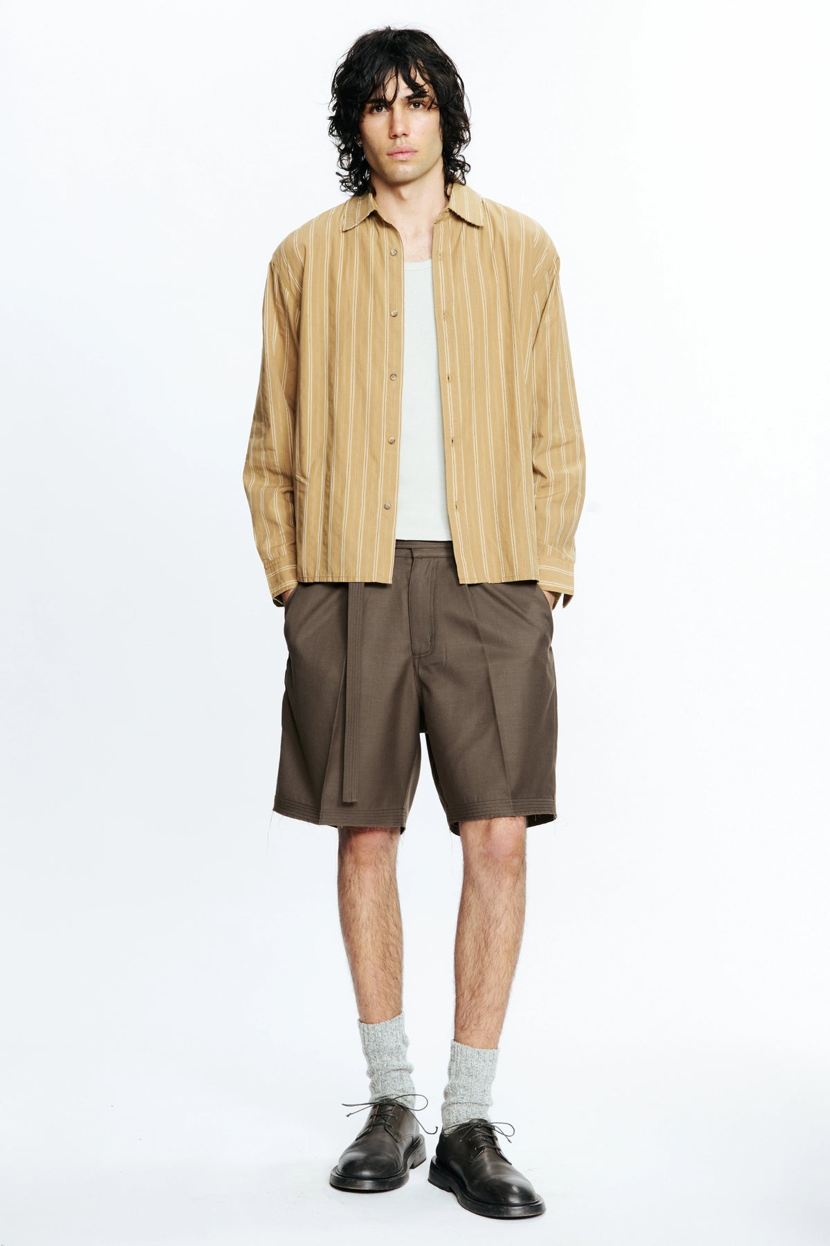 Man wearing a beige striped shirt and brown cut shorts on a white background