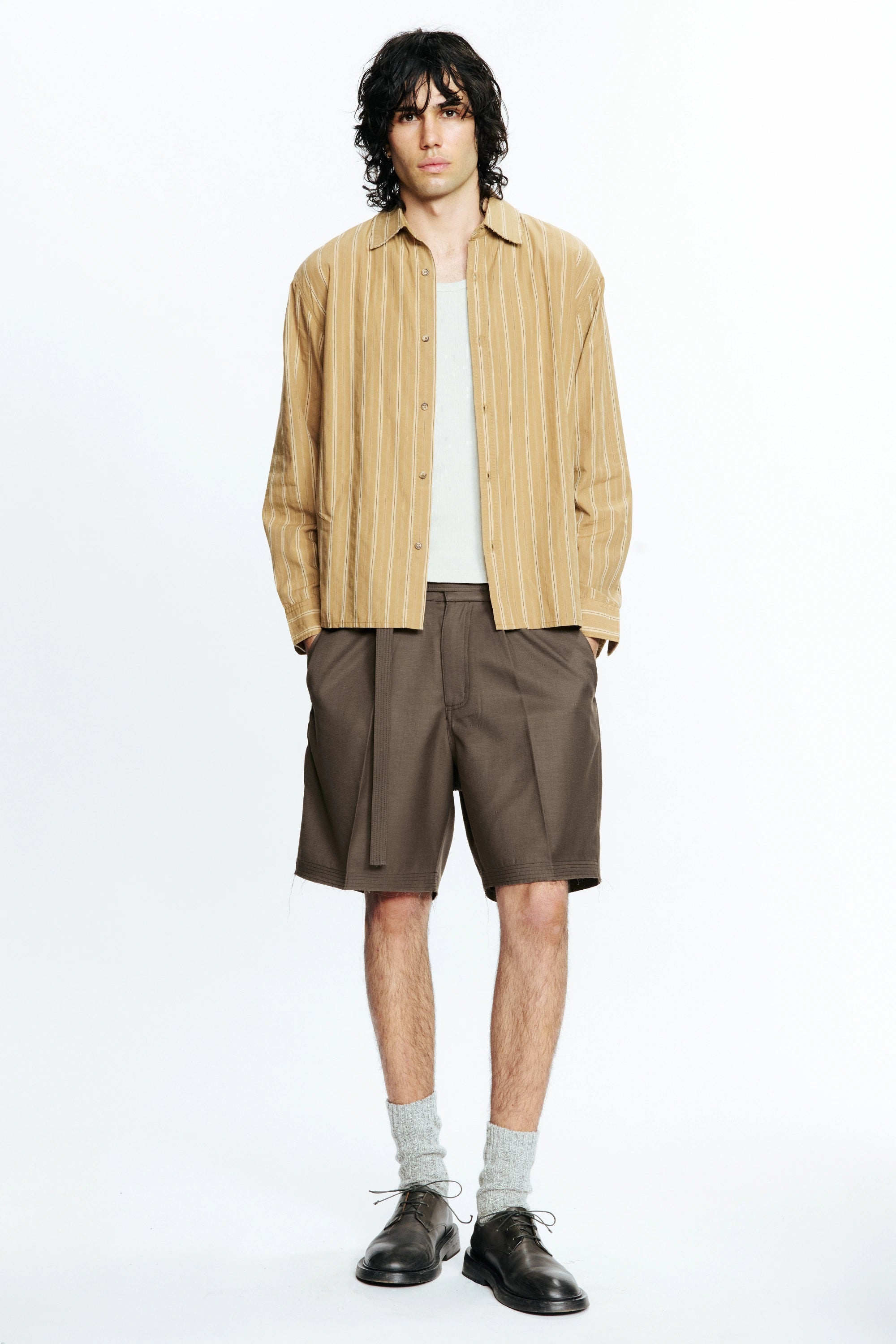 Man wearing a beige striped shirt and brown cut shorts on a white background