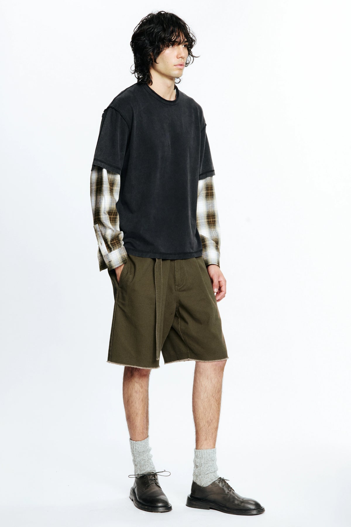 Person wearing a black t-shirt with plaid sleeves and green shorts on a white background