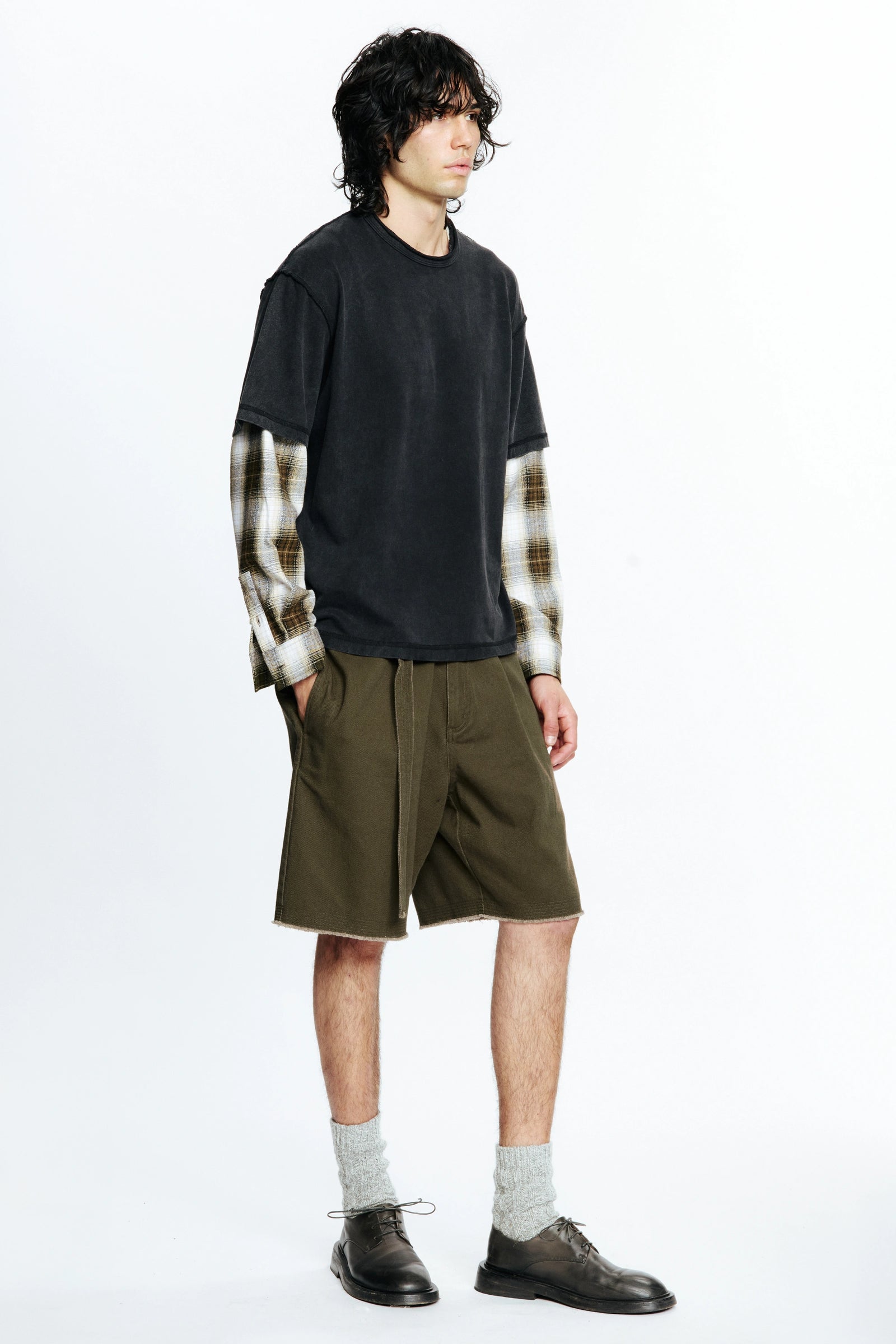 Person wearing a black t-shirt with plaid sleeves and green shorts on a white background