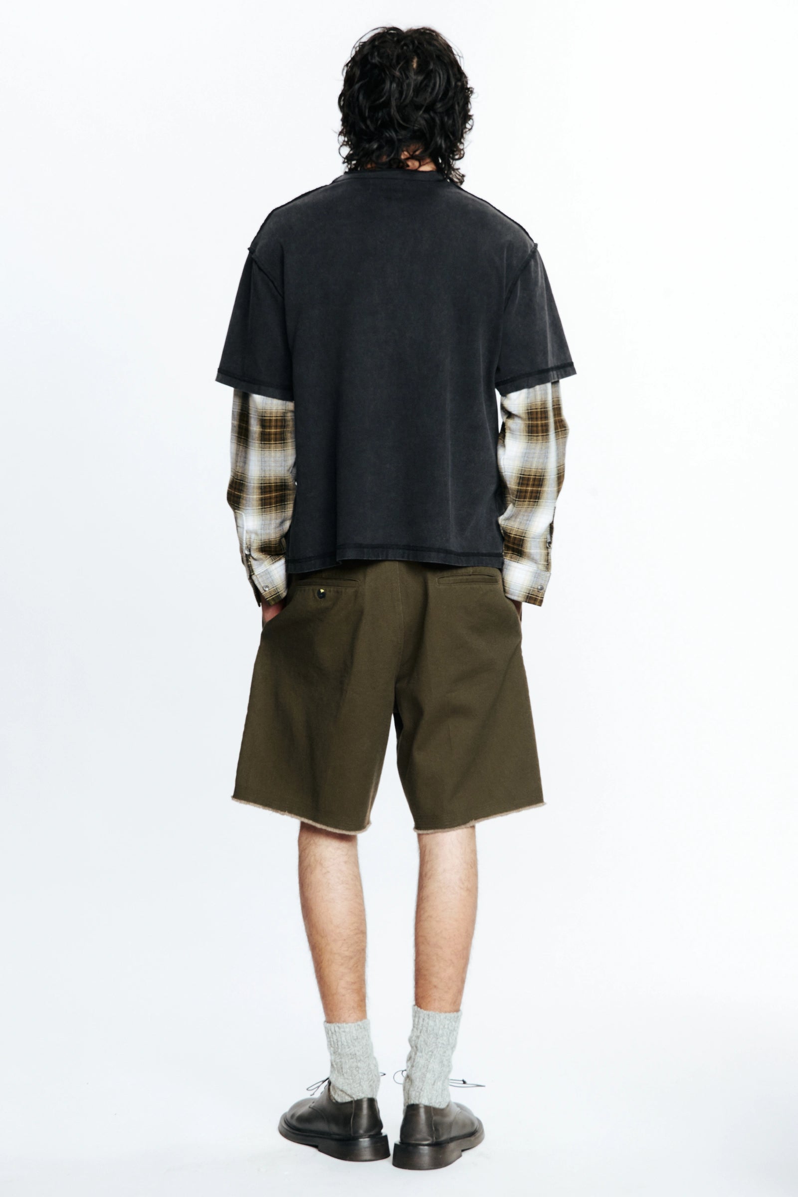 View from behind of a person wearing a black t-shirt with plaid sleeves and green shorts on a white background