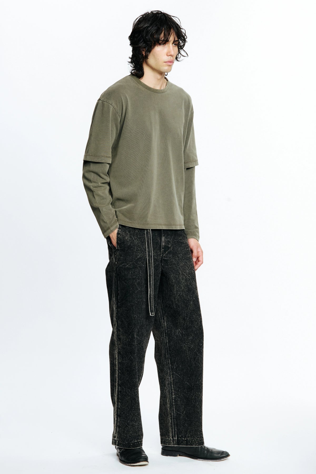 Person wearing an olive green long-sleeve shirt and black jeans on a white background