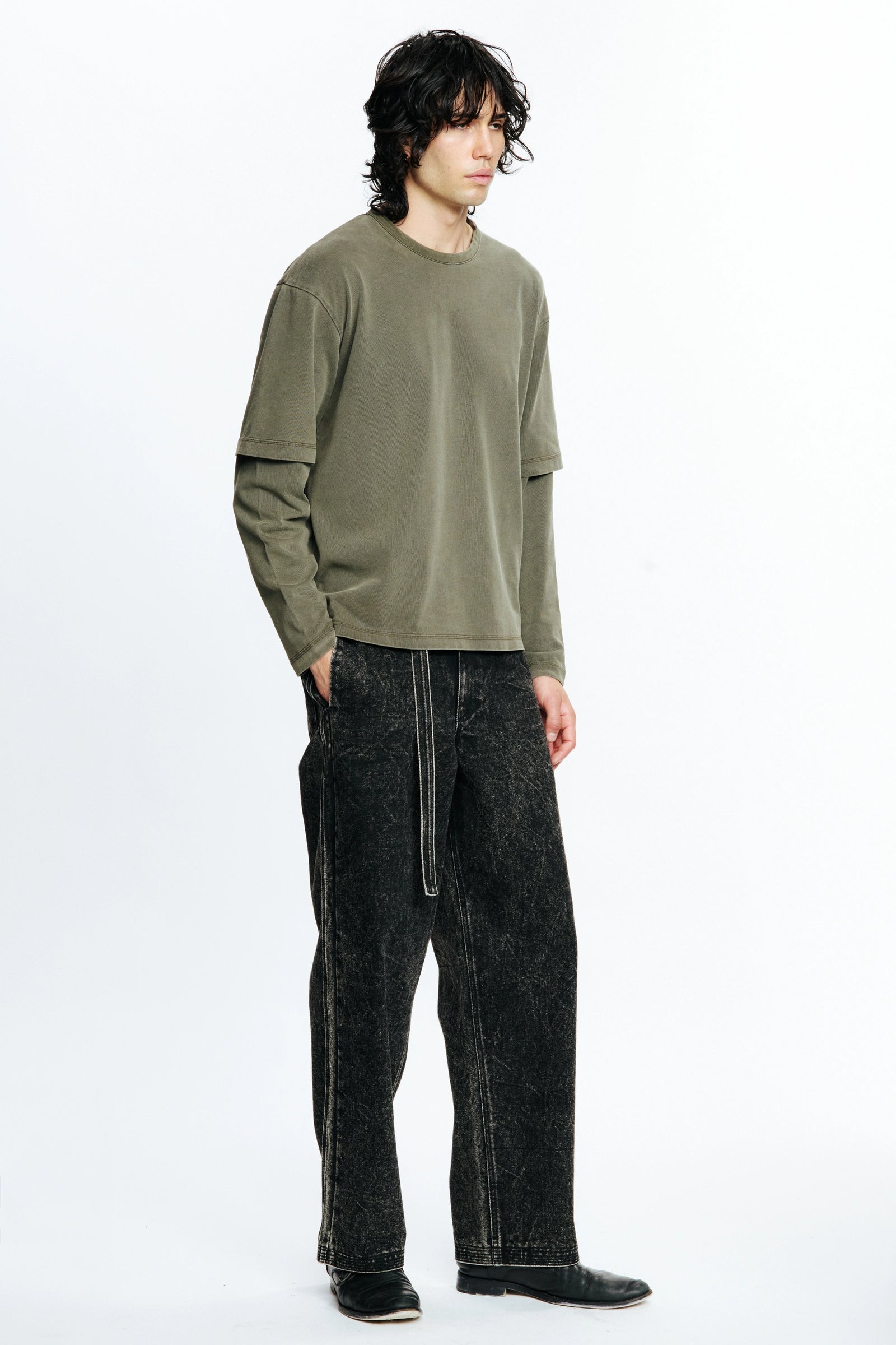 Person wearing an olive green long-sleeve shirt and black jeans on a white background
