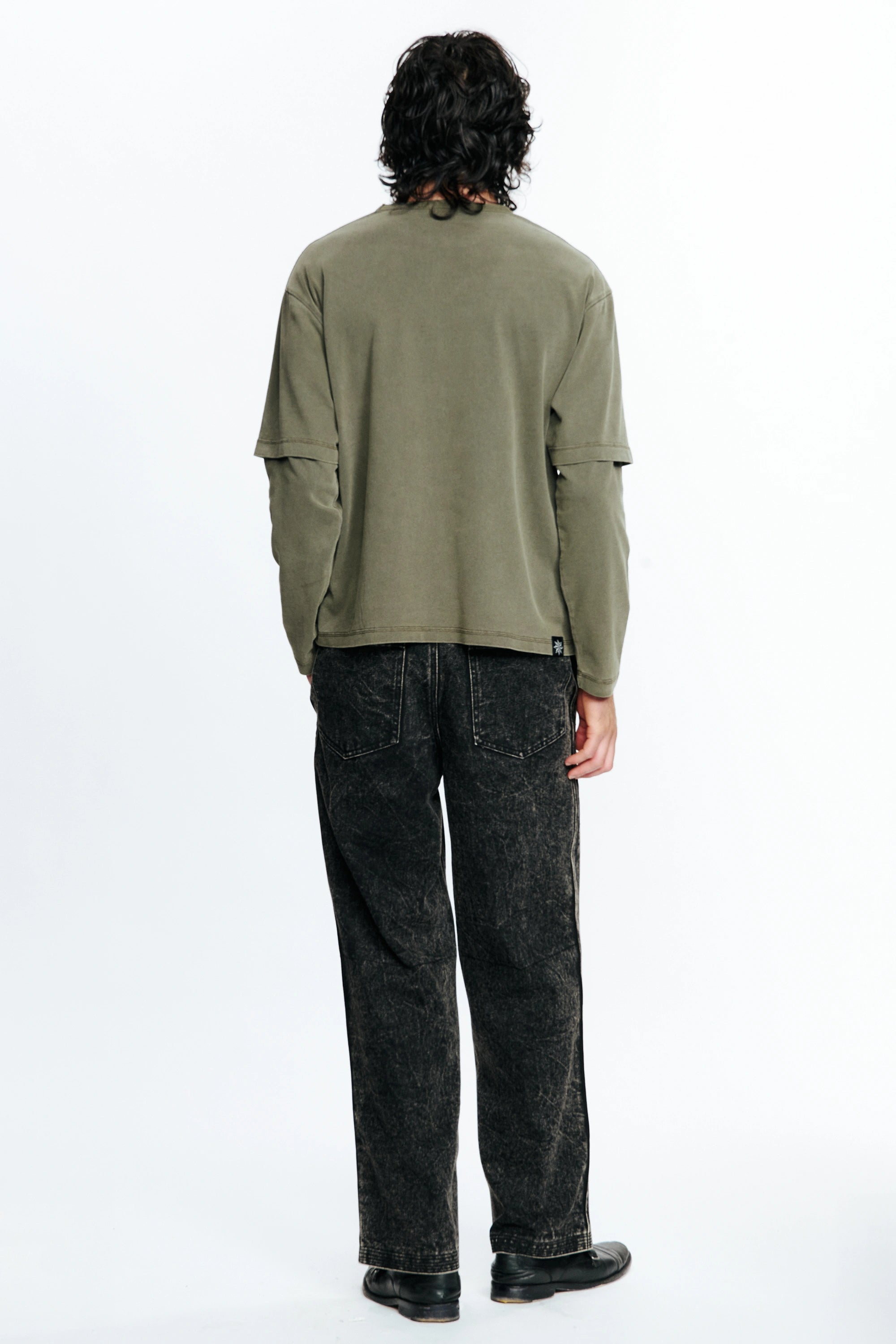 Person wearing a green shirt and dark jeans from behind on a white background