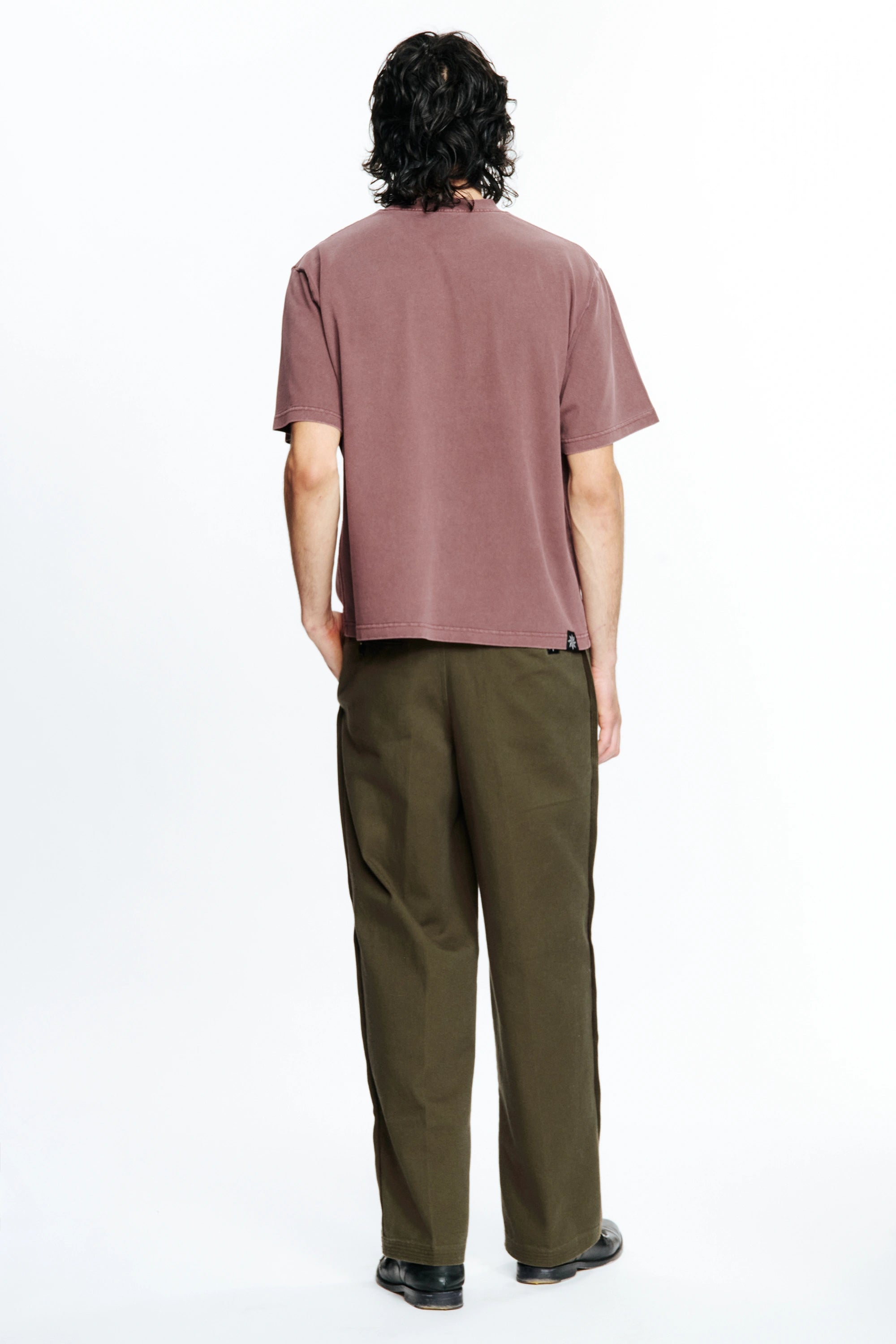 View of the back of a person wearing a mauve t-shirt and green pants on a white background
