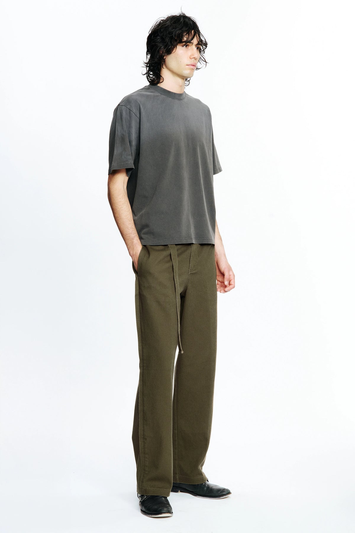 Person wearing a grey t-shirt and green pants on a white background