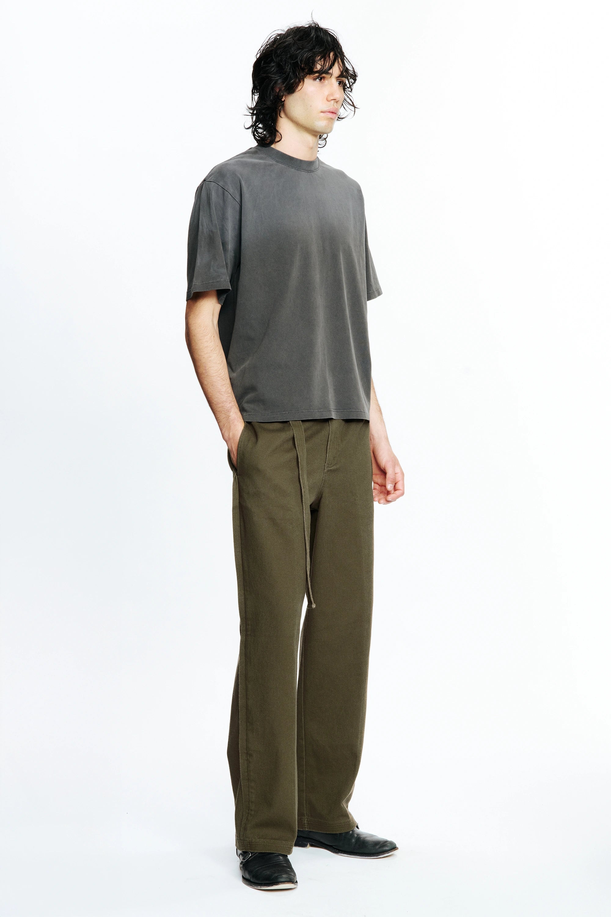 Person wearing a grey t-shirt and green pants on a white background