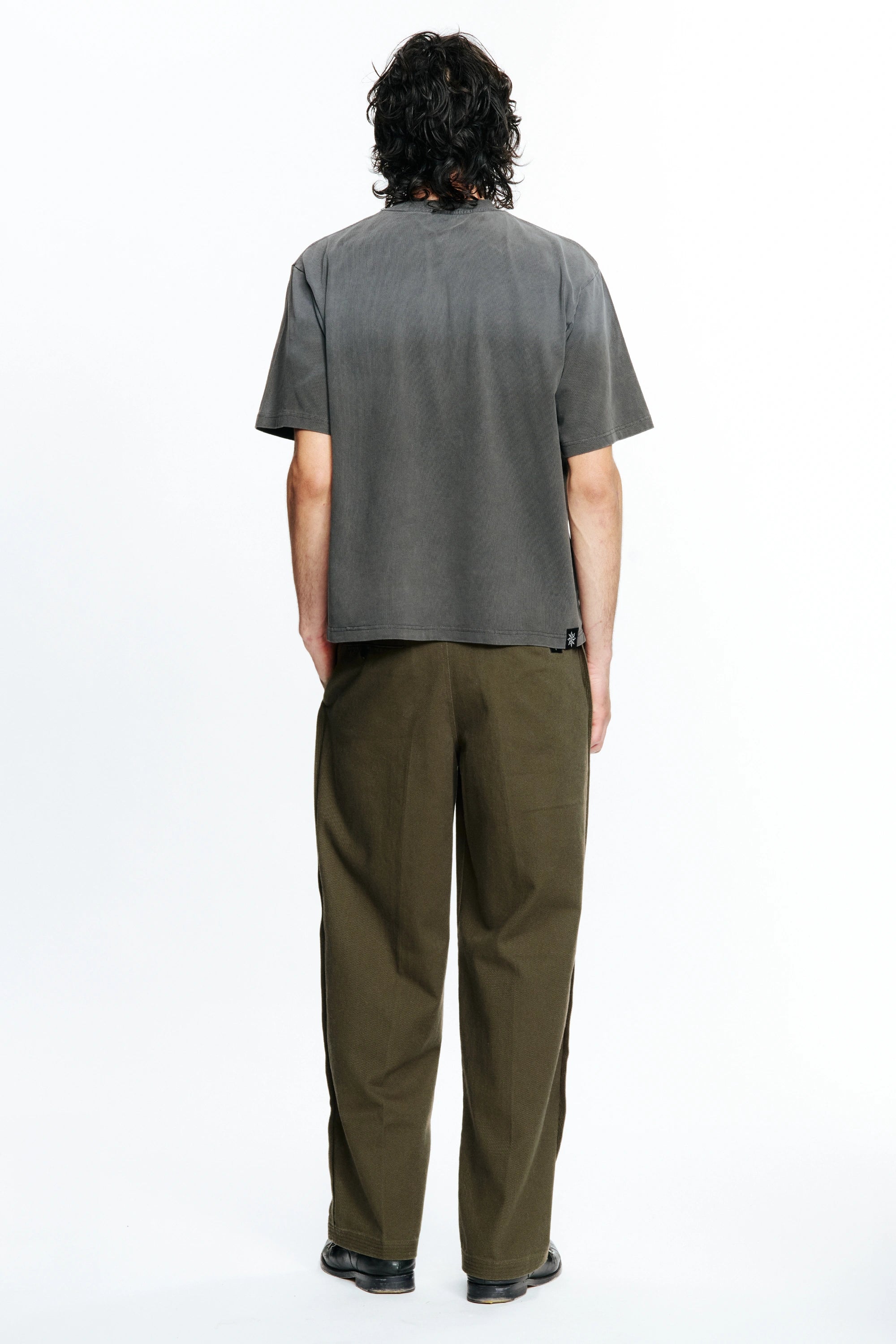 View of the back of a person  wearing a grey t-shirt and green pants on a white background