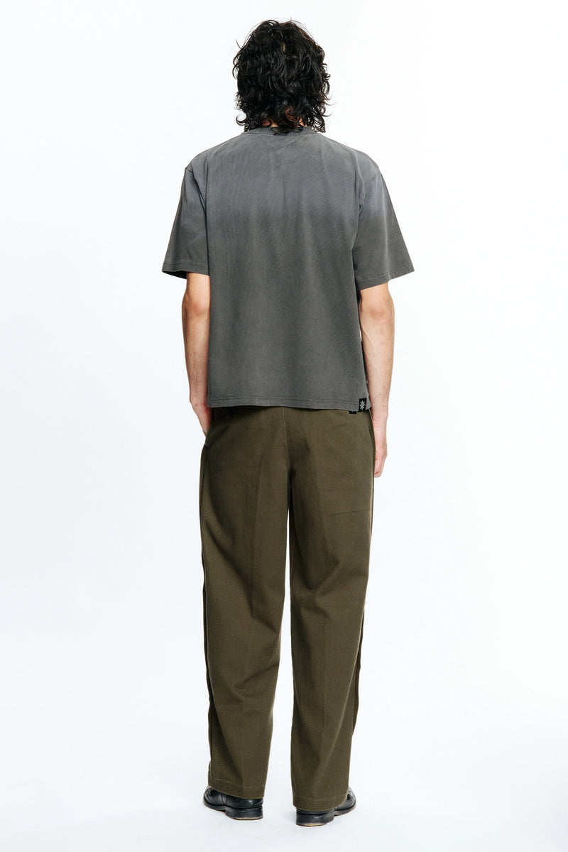 View of the back of a person  wearing a grey t-shirt and green pants on a white background