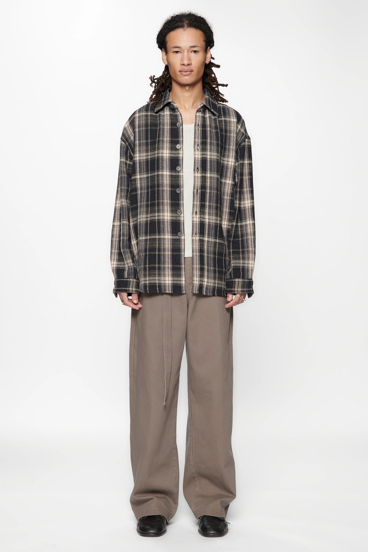 Person wearing a plaid shirt over a white shirt and beige pants on a white background