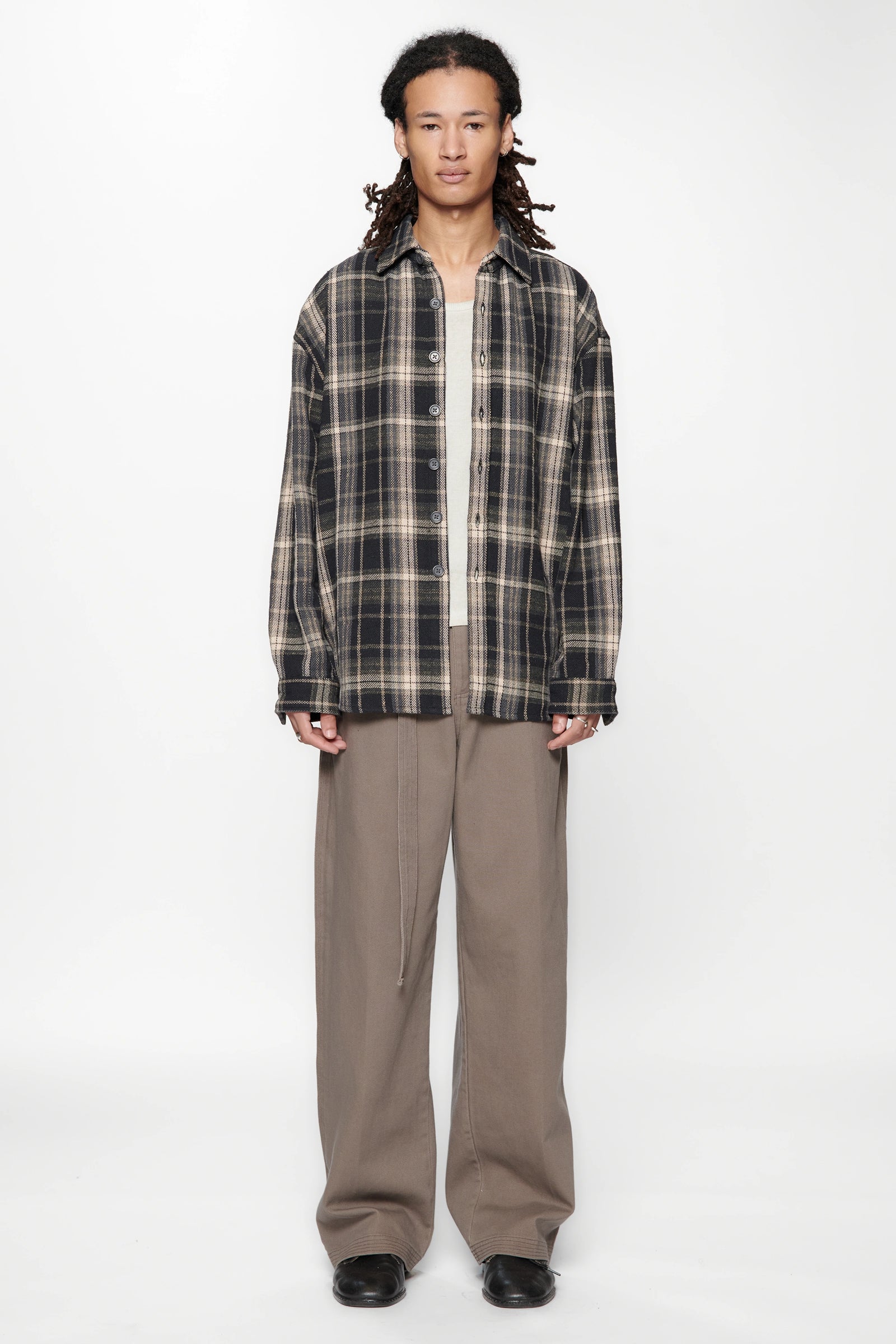 Person wearing a plaid shirt over a white shirt and beige pants on a white background