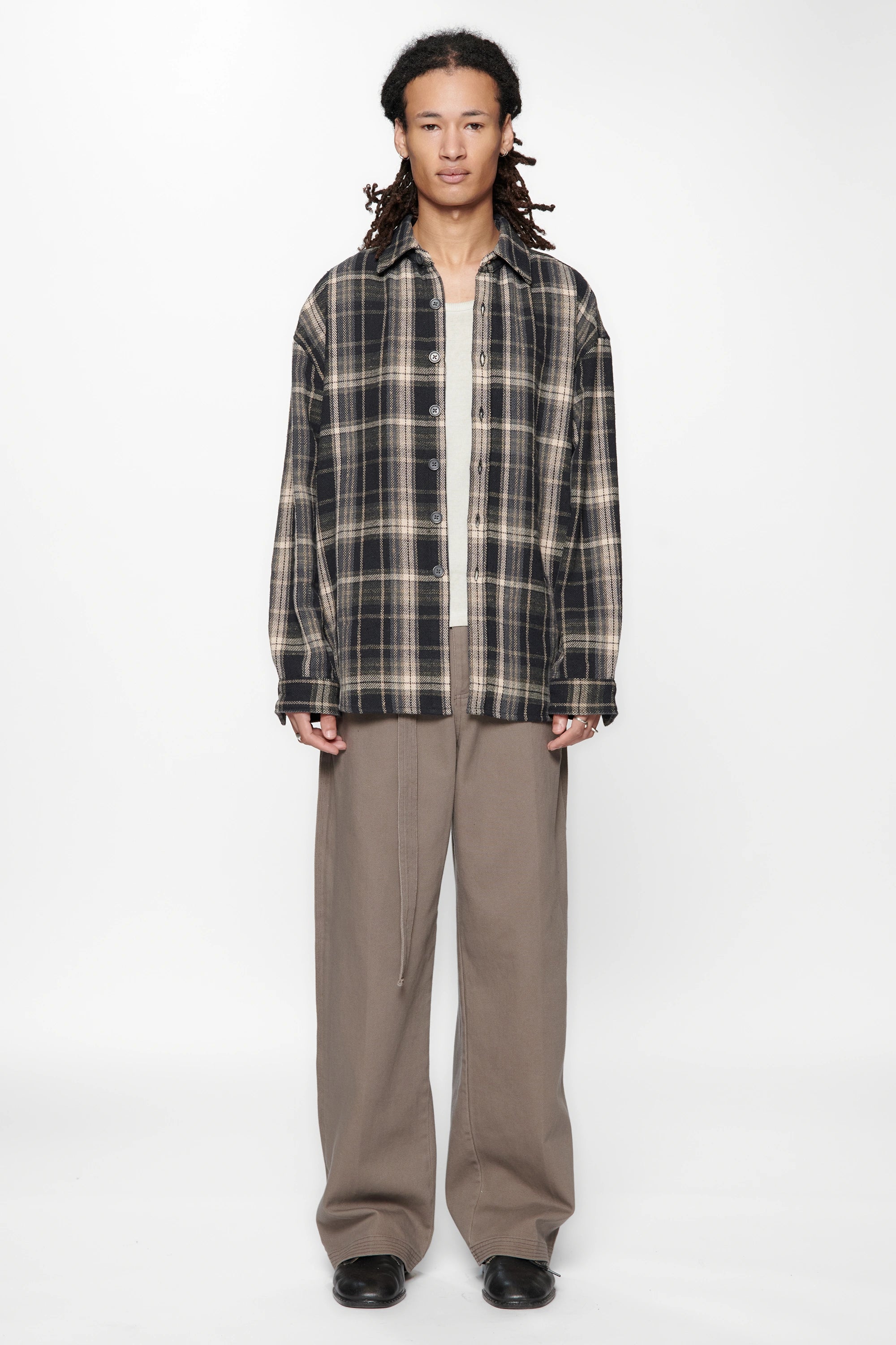 Person wearing a plaid shirt over a white shirt and beige pants on a white background