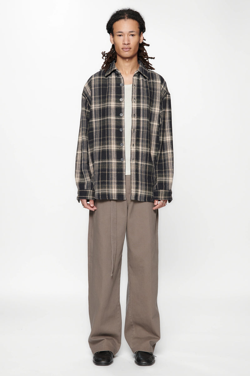 Person wearing a plaid shirt over a white shirt and beige pants on a white background