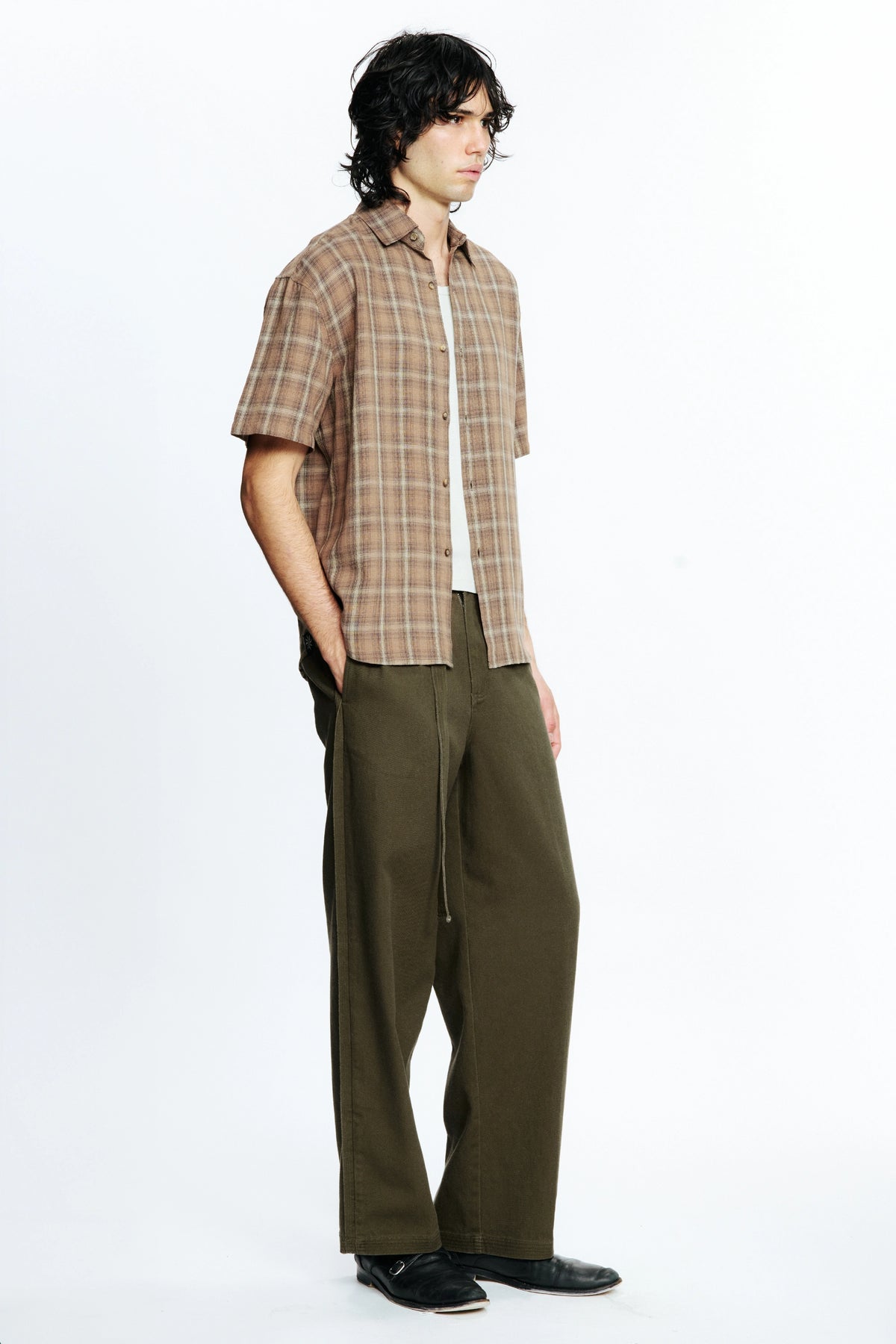 View from the side of a person wearing a Brown Checkered Drop Short Sleeve Shirt and olive green pants on a white background