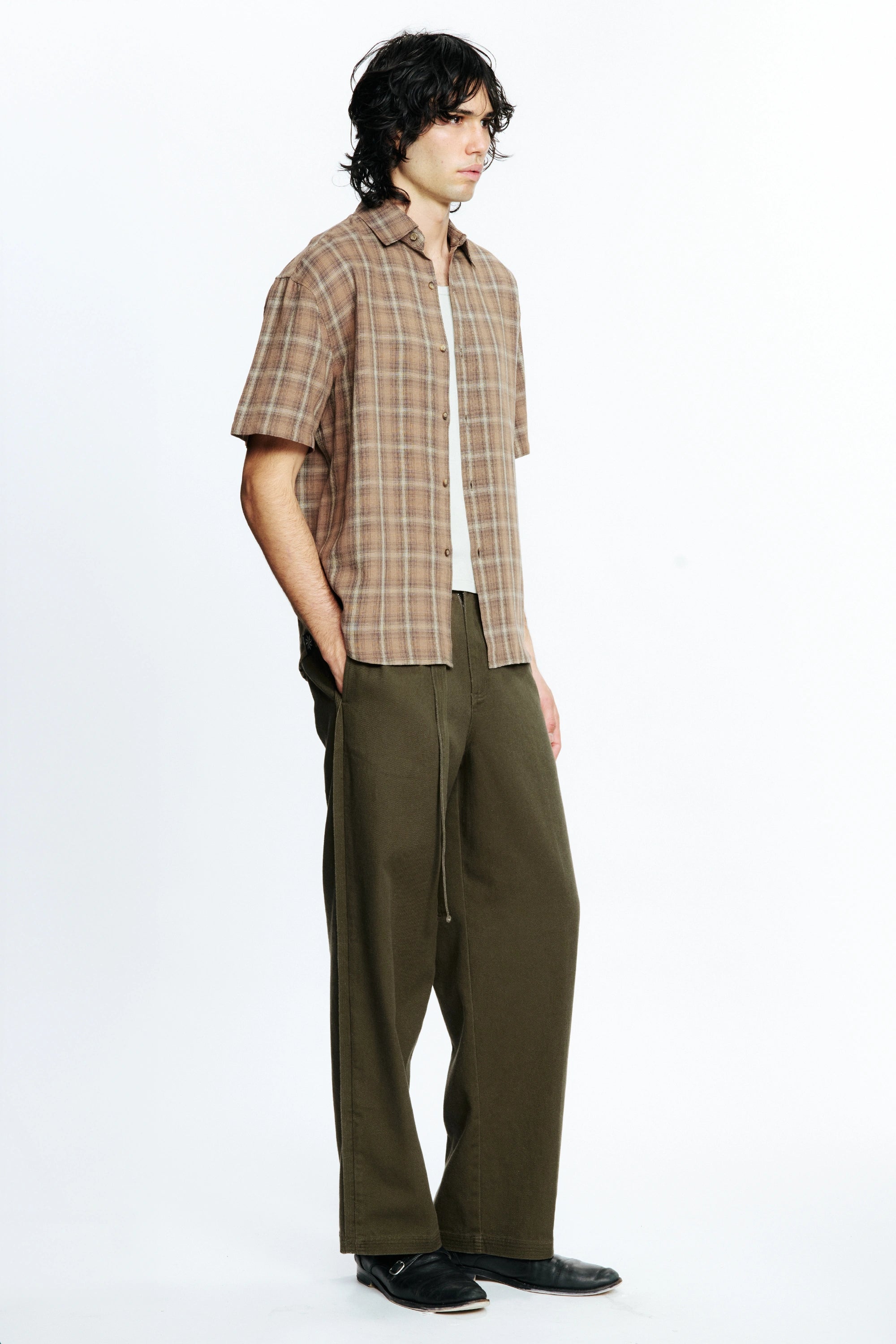 View from the side of a person wearing a Brown Checkered Drop Short Sleeve Shirt and olive green pants on a white background