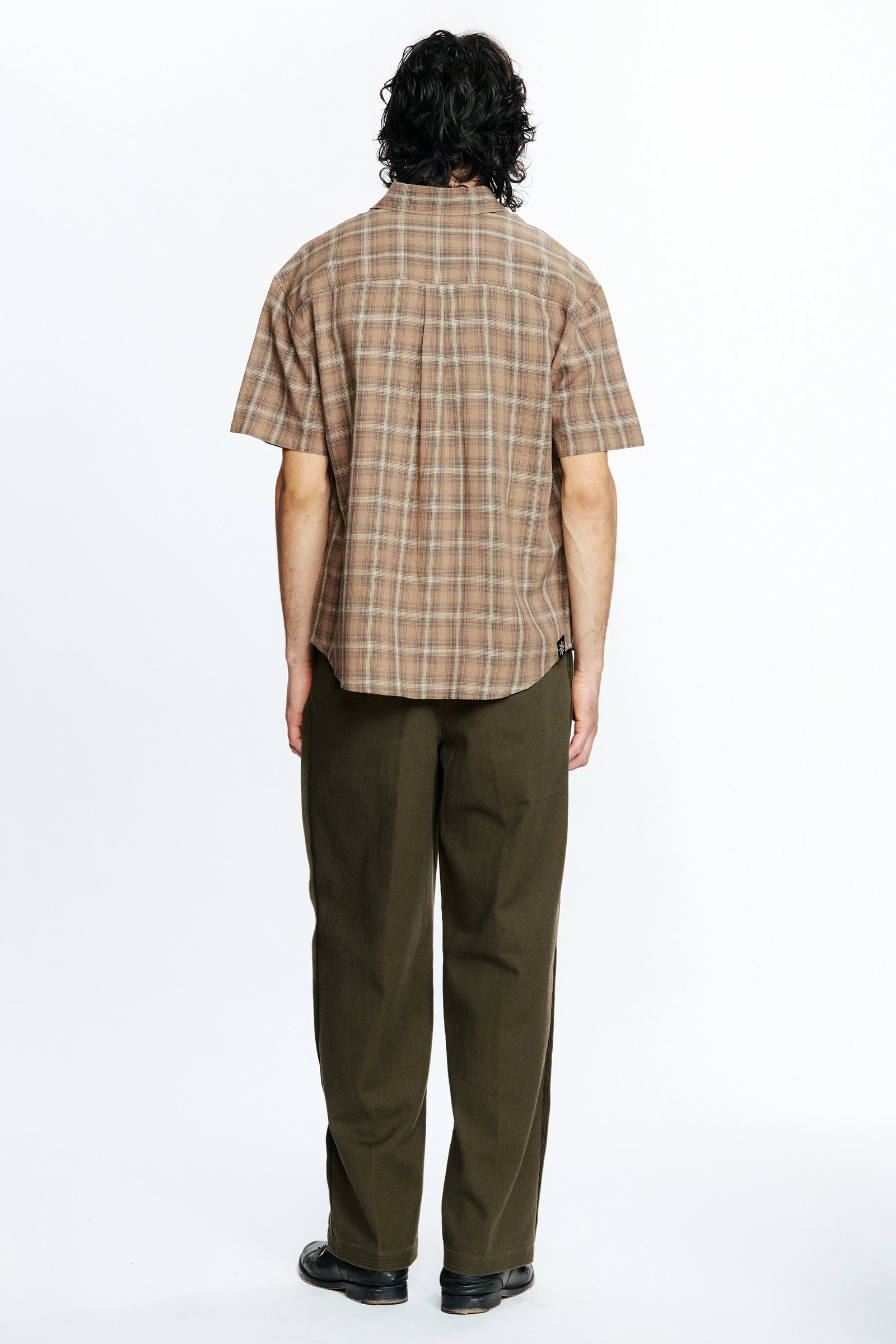 View from behind of a person wearing a Brown Checkered Drop Short Sleeve Shirt and green pants on a white background