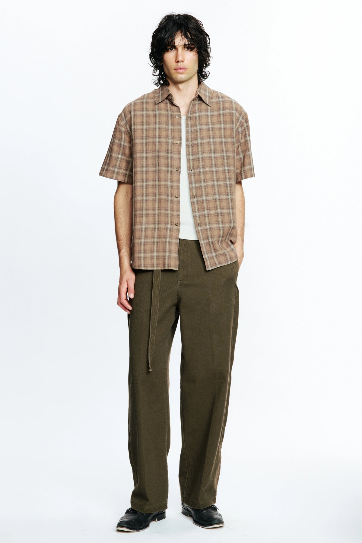 Person wearing a brown plaid shirt and olive green pants on a white background