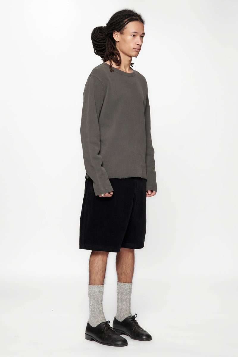 Person wearing a grey sweater, black shorts, and black shoes on a white background