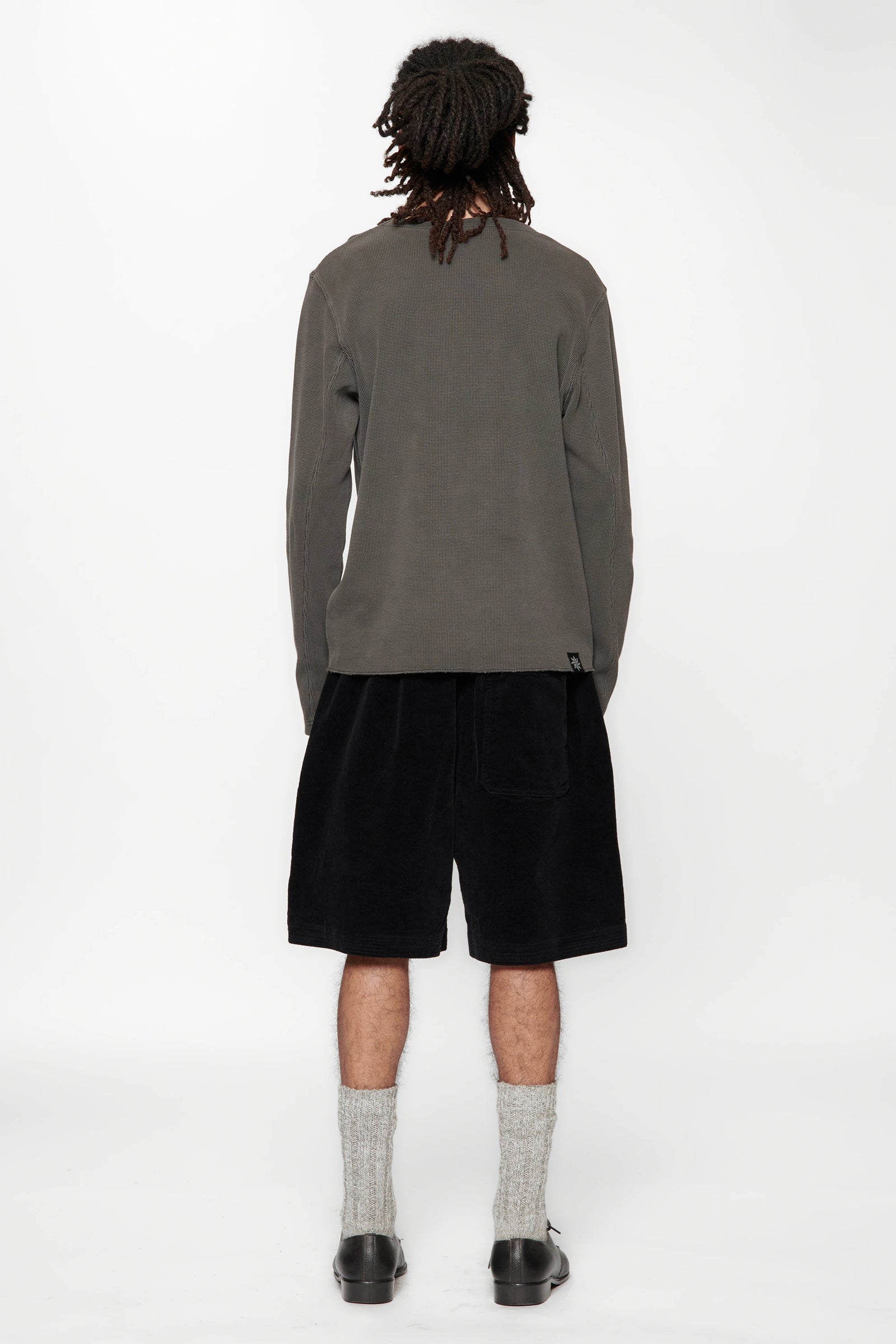Person with their back turned wearing a grey long-sleeve shirt and black shorts on a white background
