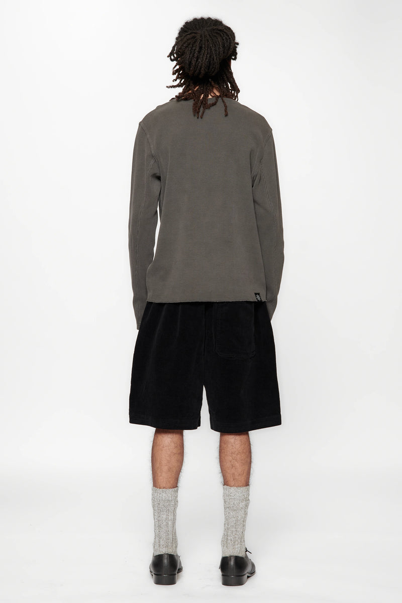 Person with their back turned wearing a grey long-sleeve shirt and black shorts on a white background
