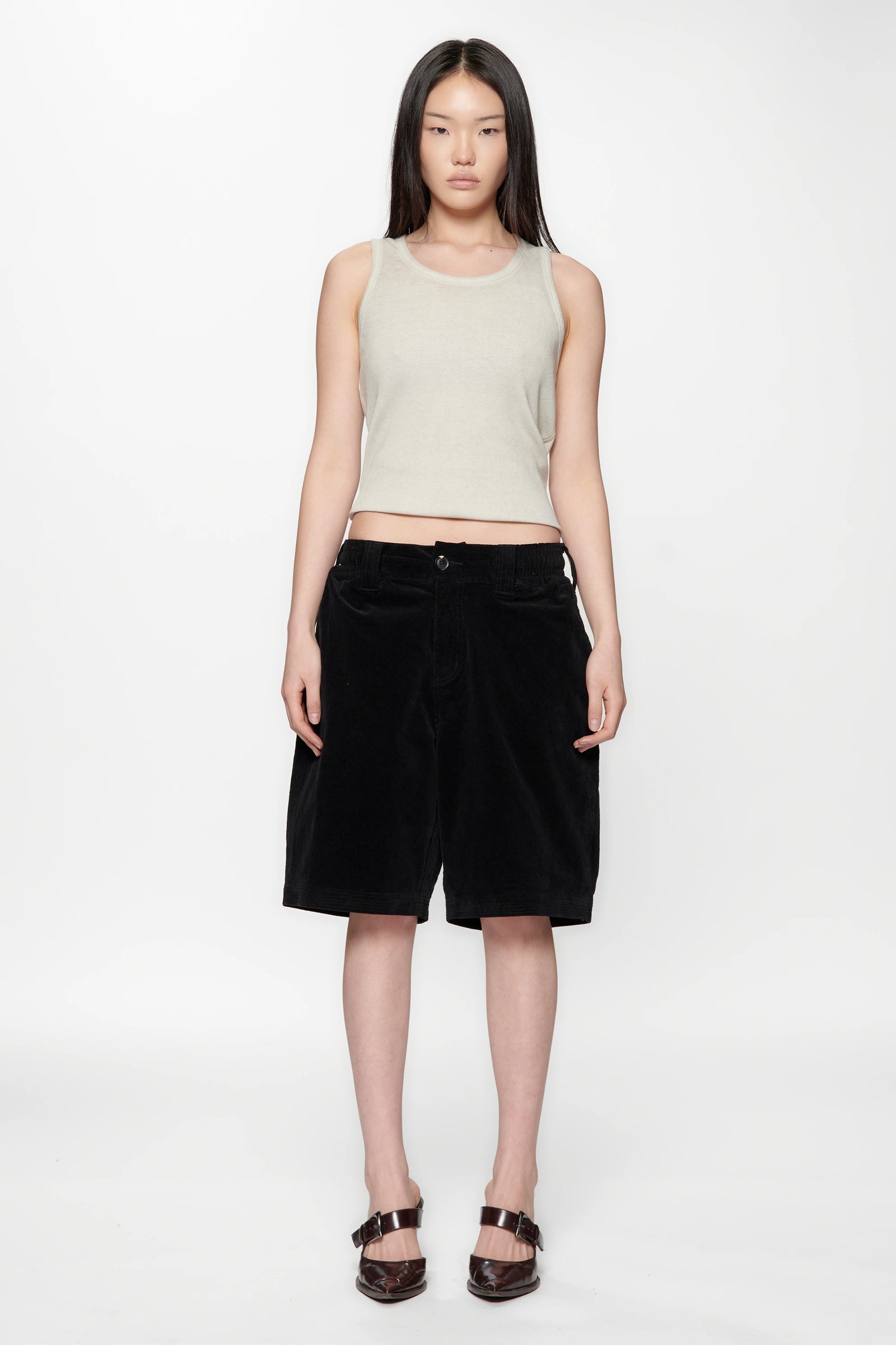 Woman wearing a light beige sleeveless top and black shorts on a white background