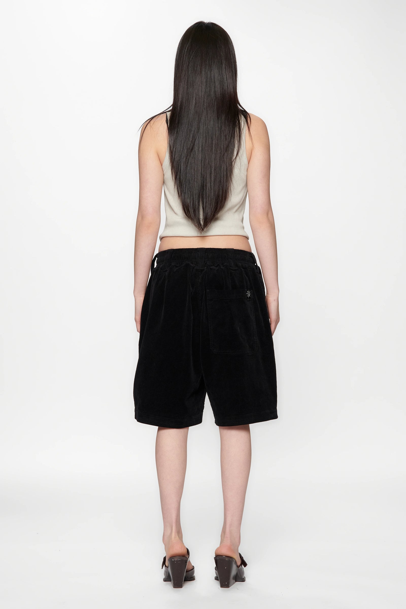 View from behind of a woman wearing a beige top and black shorts on a white background