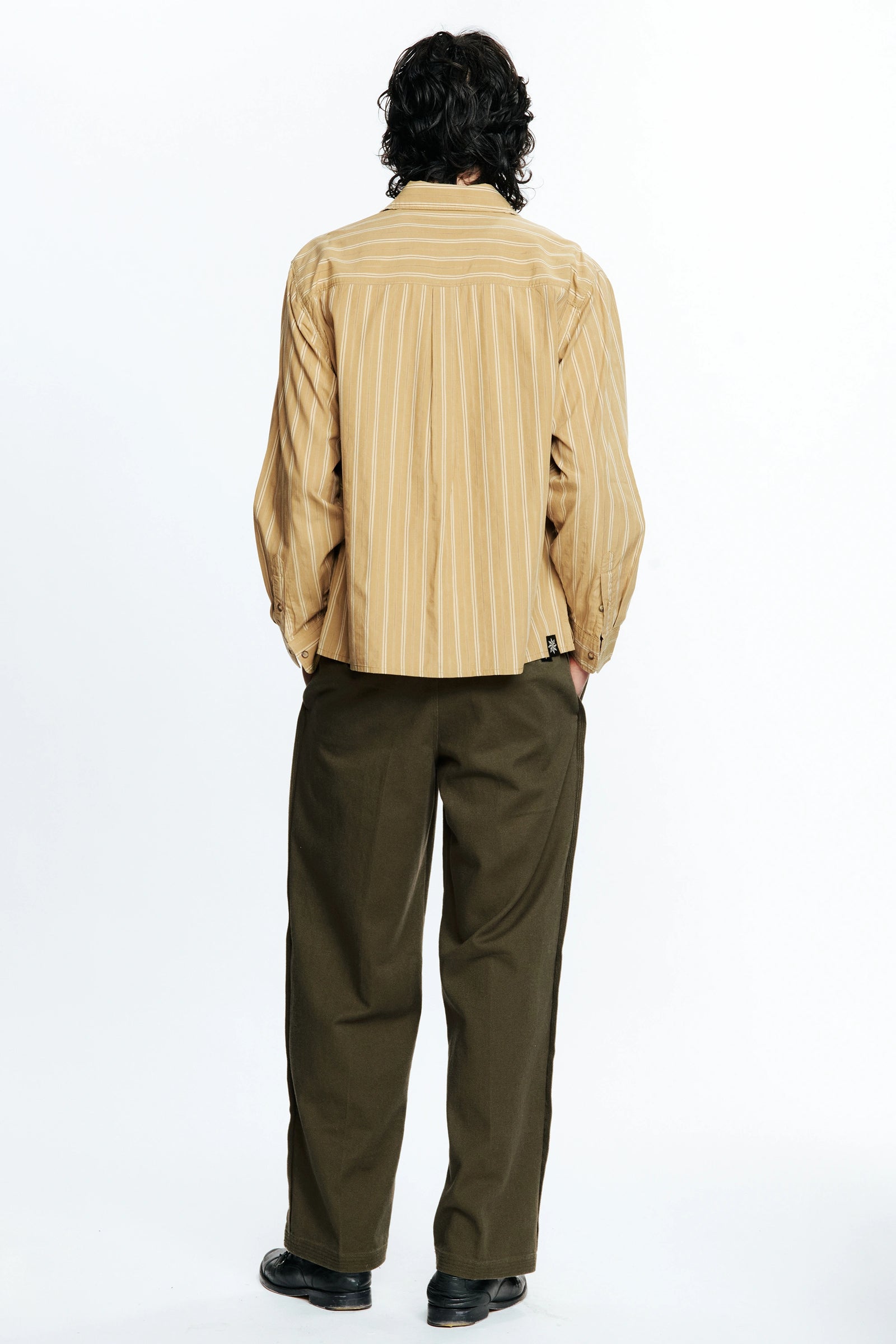 Person with their back turned wearing a Tan Stripe Hold Long Sleeve Shirt and green pants on a white background