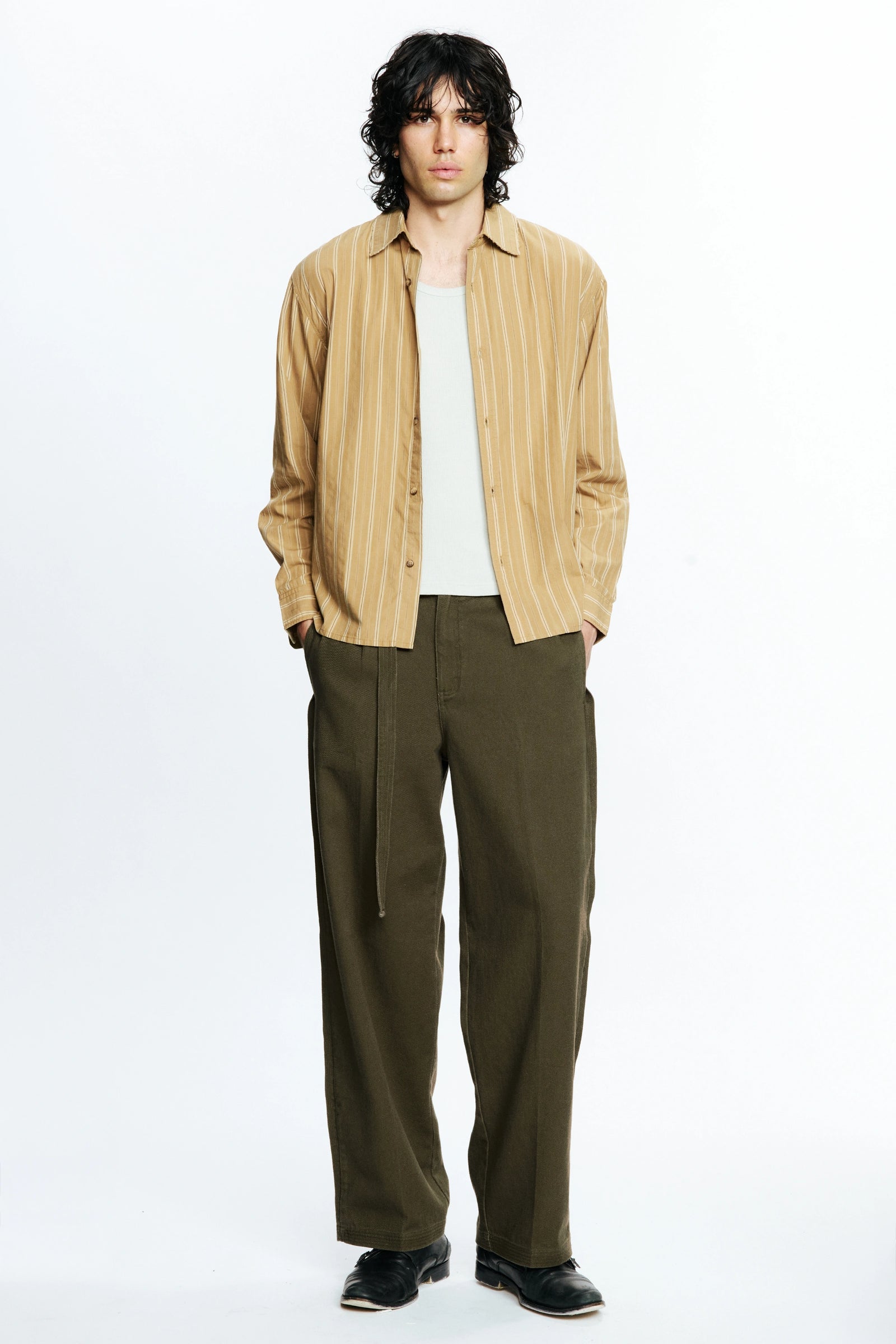 Man wearing a beige striped shirt, white t-shirt and olive green pants on a white background