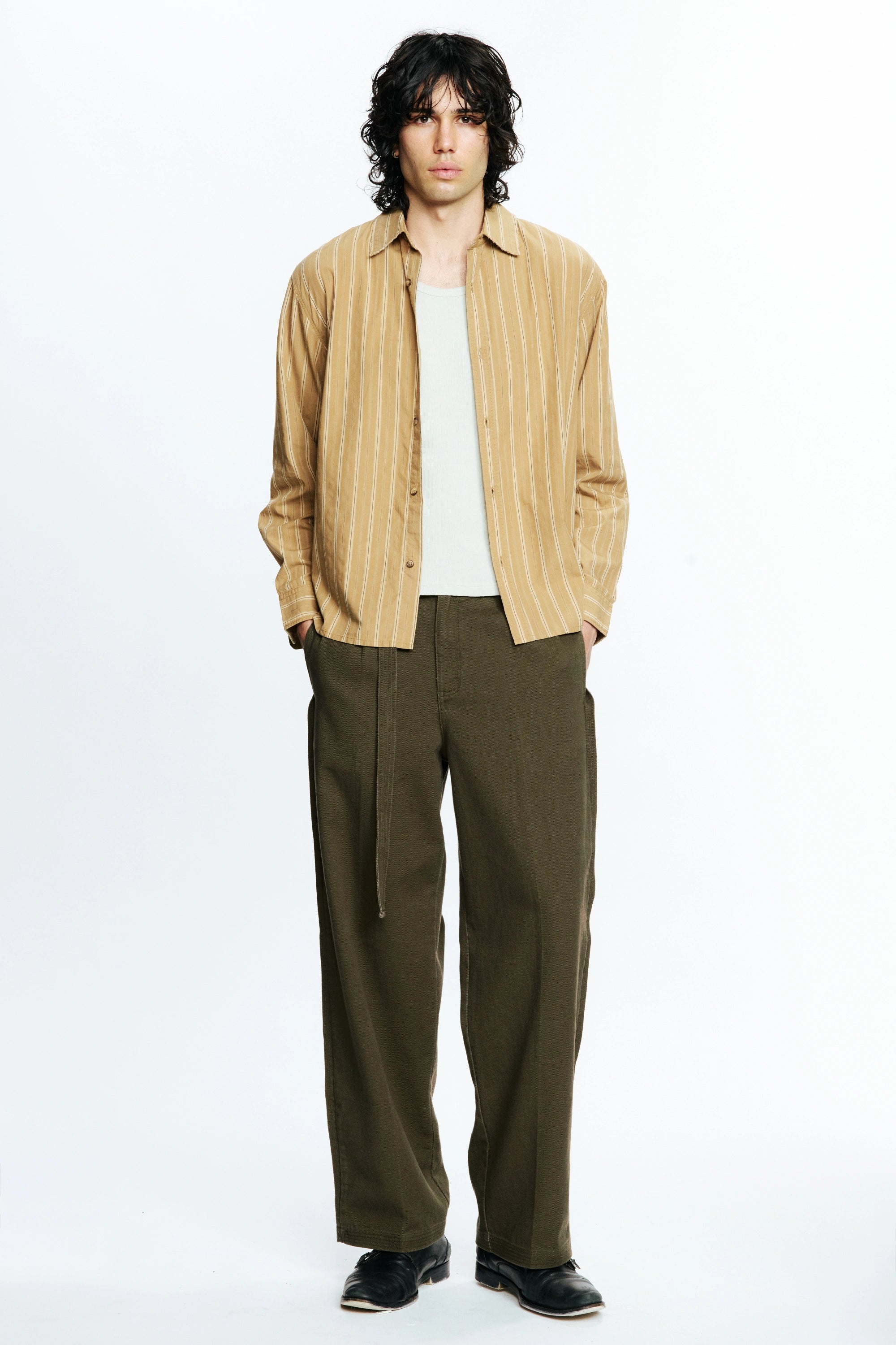 Man wearing a beige striped shirt, white t-shirt and olive green pants on a white background