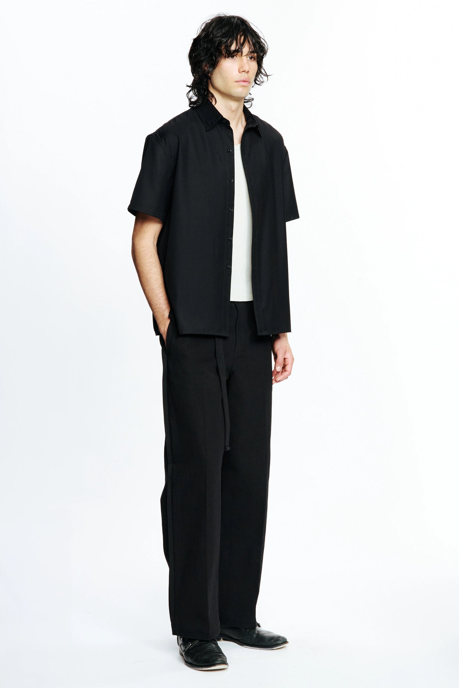 Person facing to one side wearing a Black Hold Short Sleeve Shirt and dark trousers on a white background