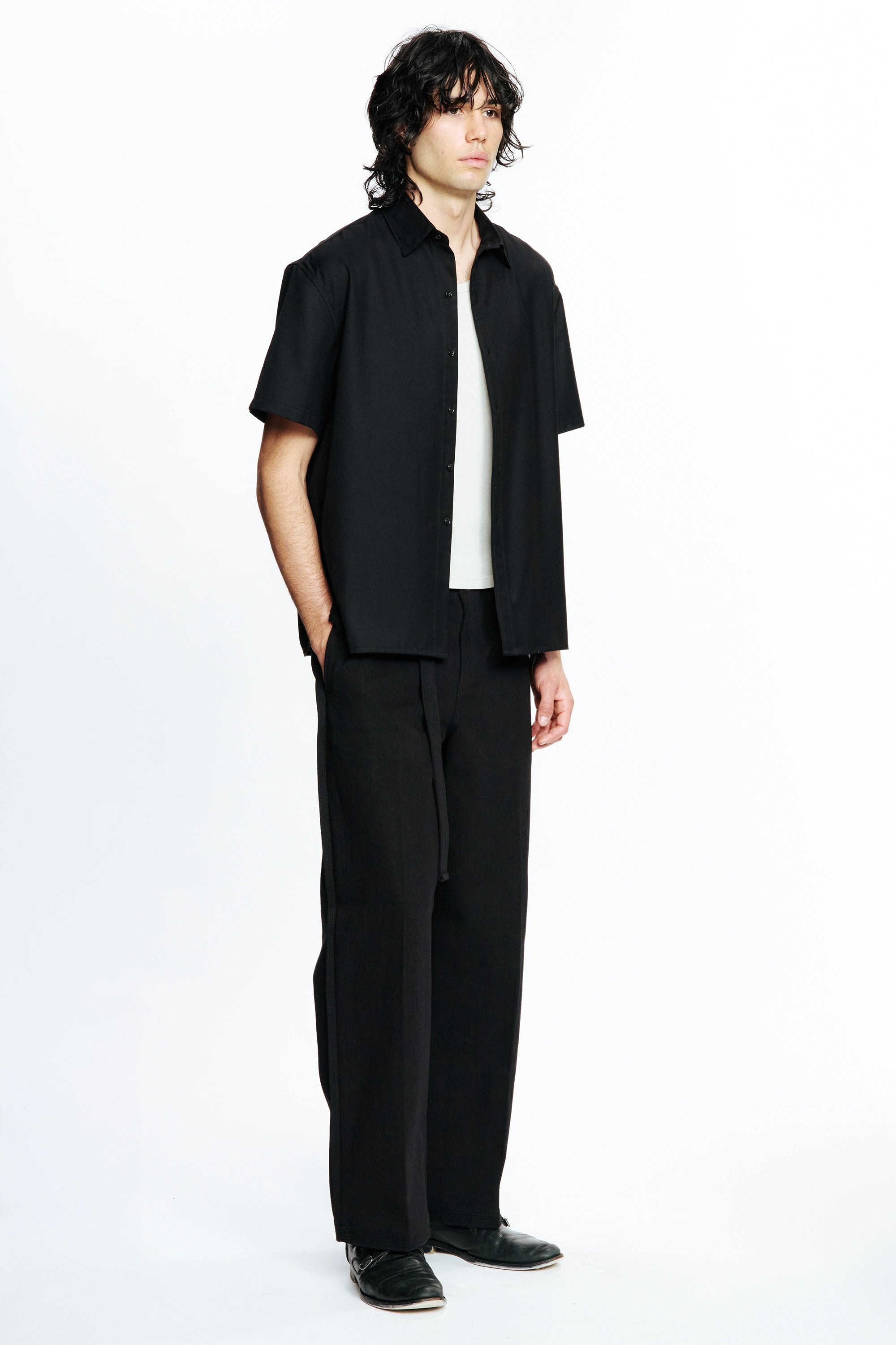 Person facing to one side wearing a Black Hold Short Sleeve Shirt and dark trousers on a white background