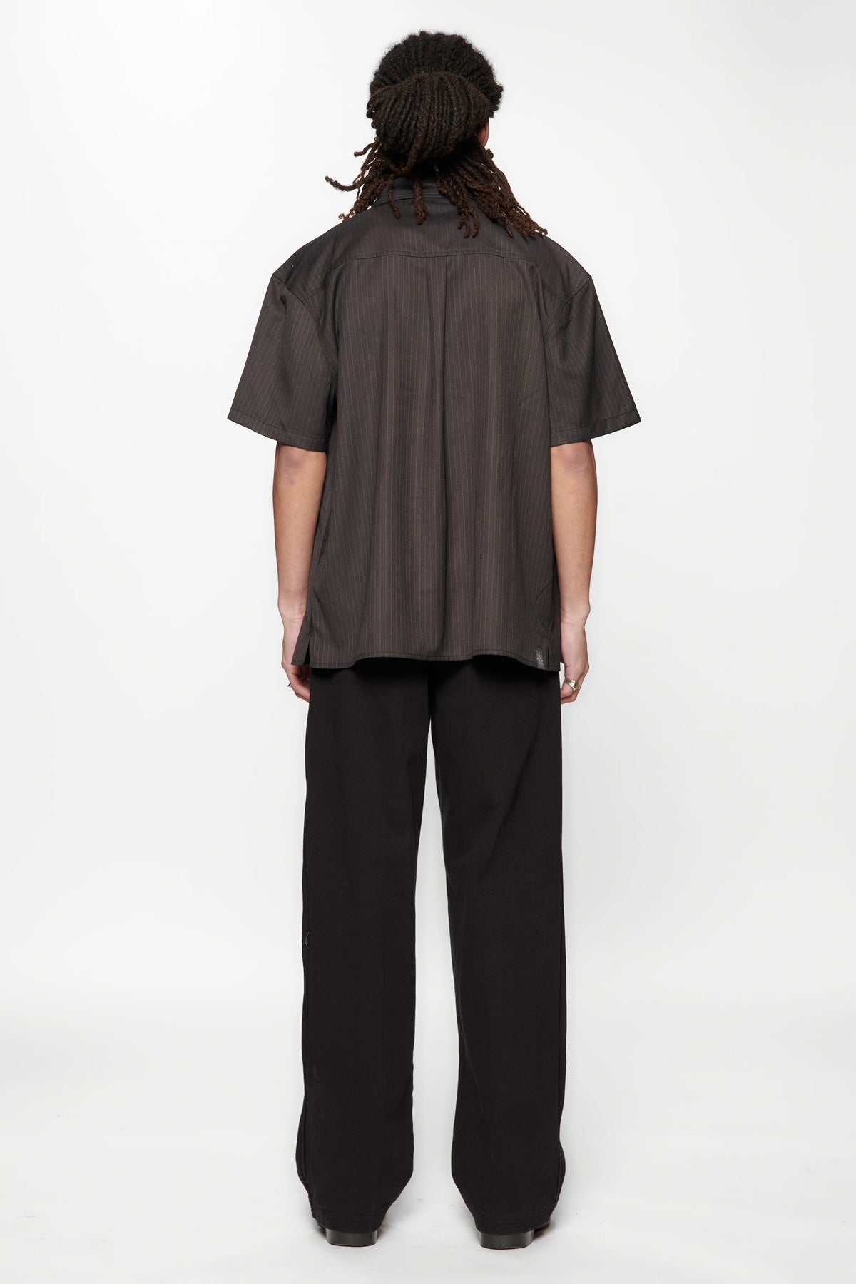 Rear view of a person wearing a dark brown shirt and black pants on a white background