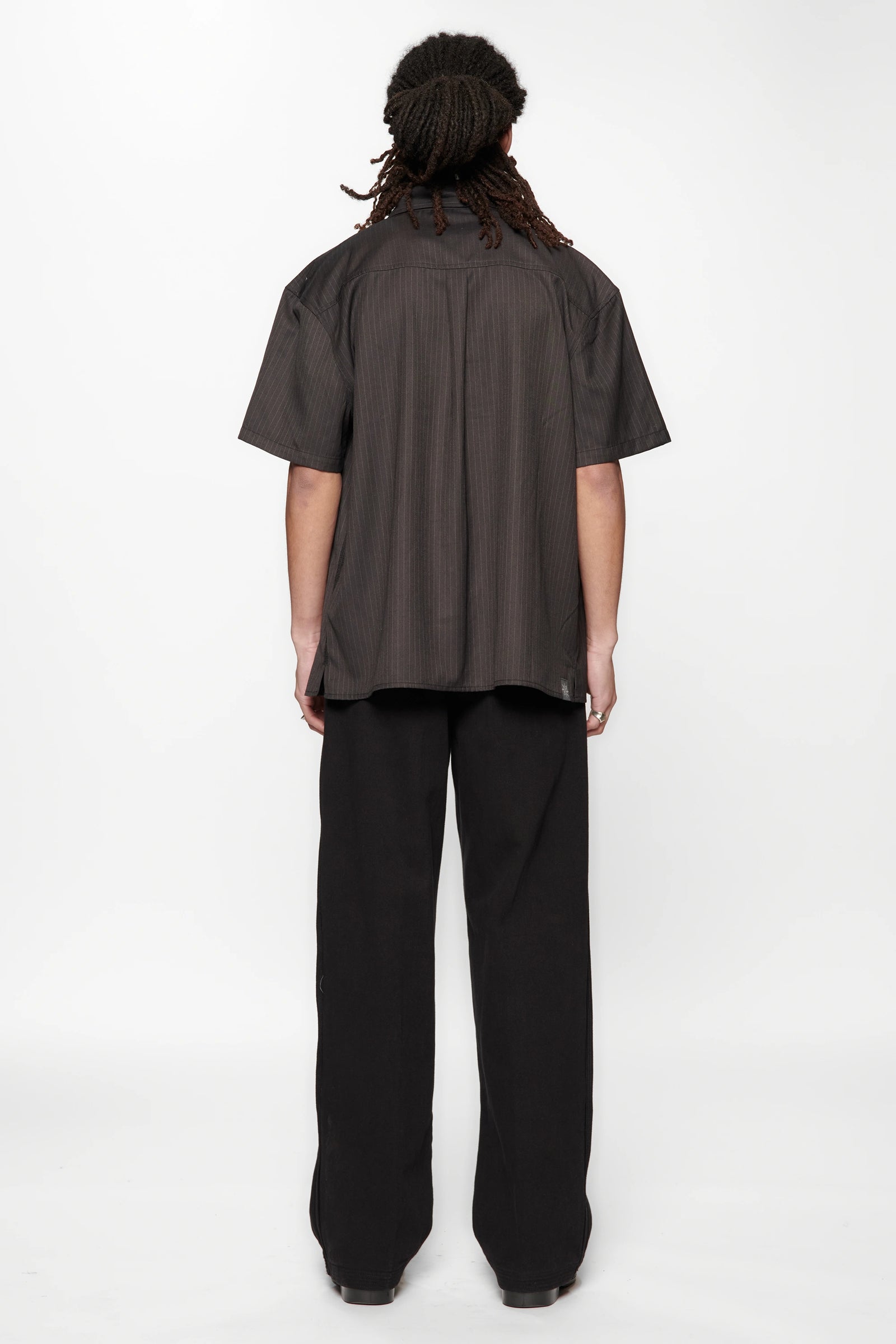 Rear view of a person wearing a dark brown shirt and black pants on a white background