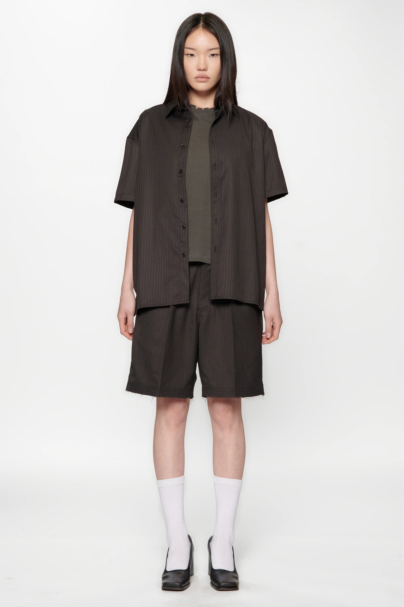 A female model wearing a Classic Pinstripe Hold Short Sleeve Shirt with dark shorts on a white background