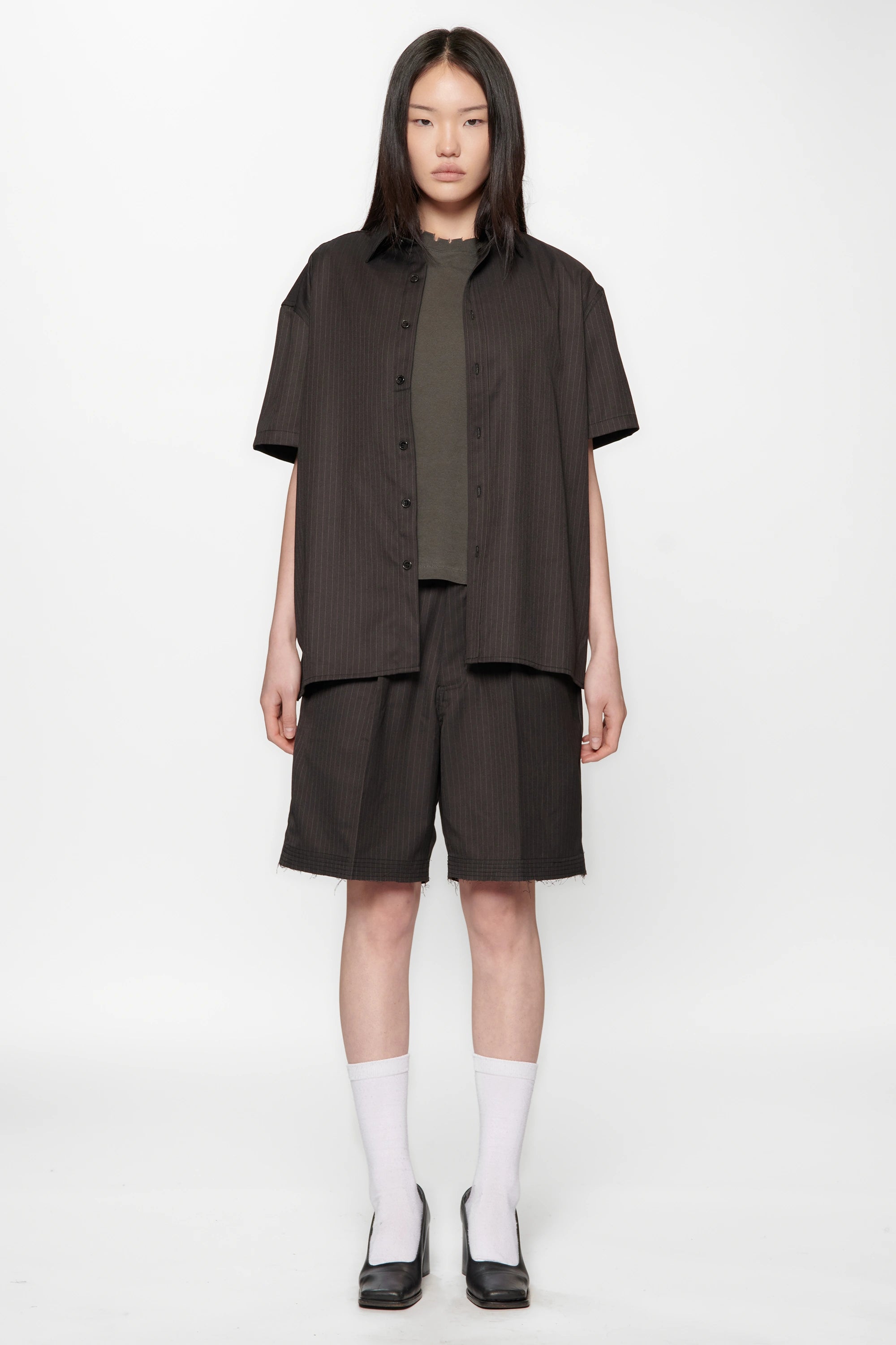 A female model wearing a Classic Pinstripe Hold Short Sleeve Shirt with dark shorts on a white background