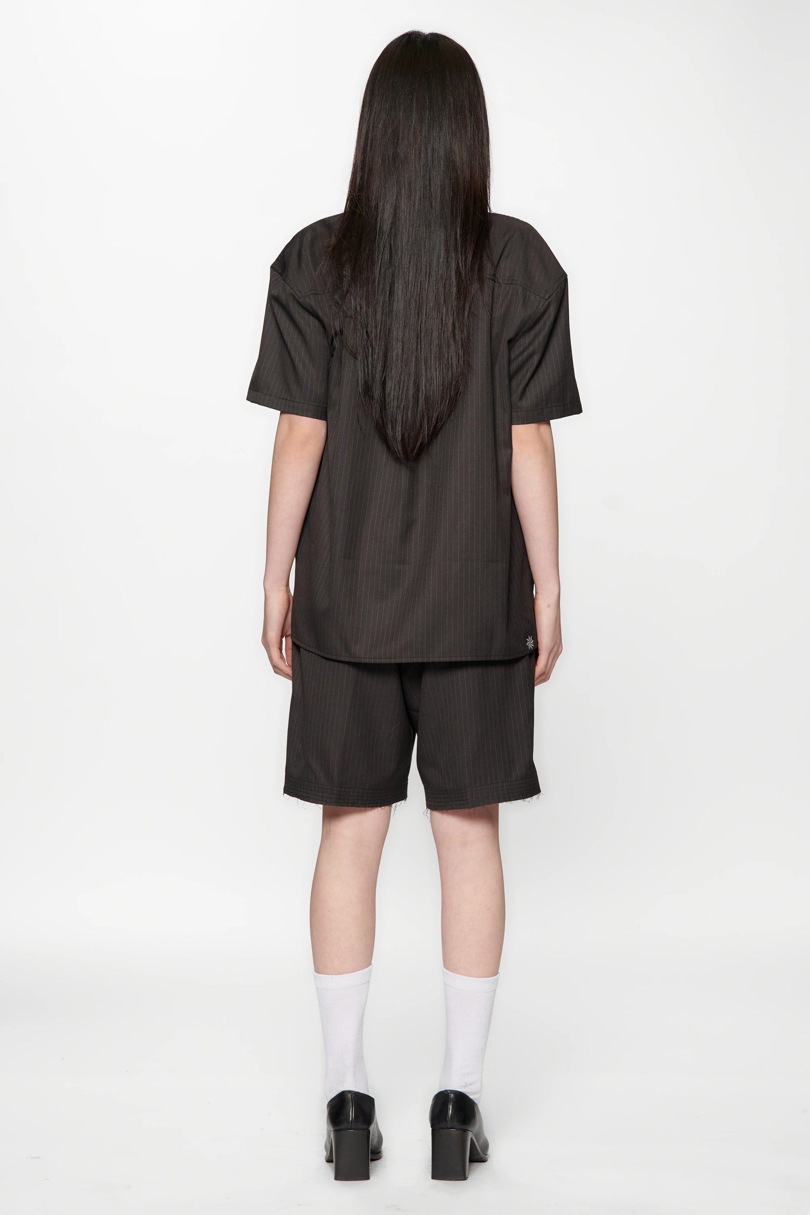 Woman with her back turned wearing a Classic Pinstripe Hold Short Sleeve Shirt and dark shorts on a white background