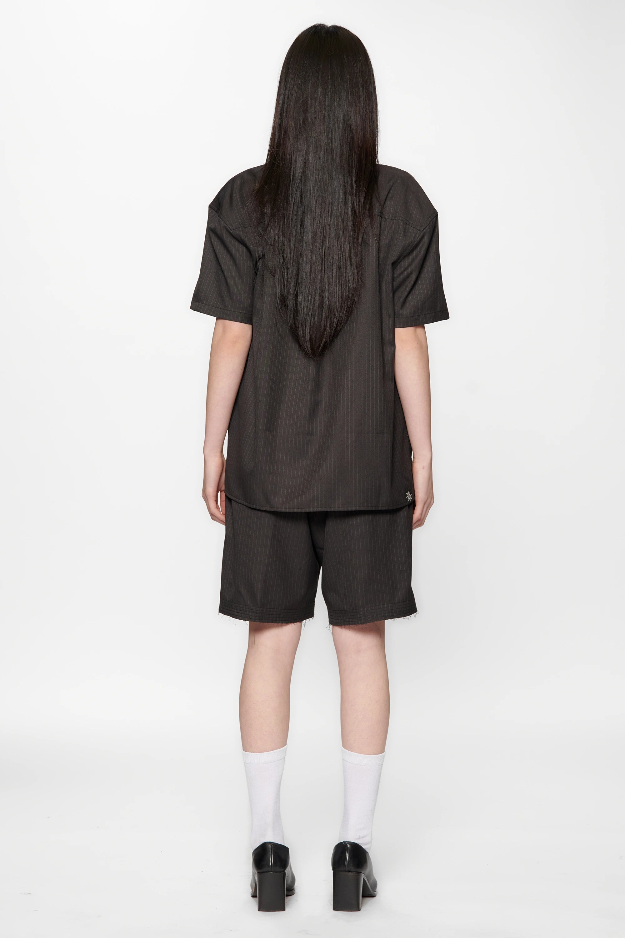 Woman with her back turned wearing a Classic Pinstripe Hold Short Sleeve Shirt and dark shorts on a white background