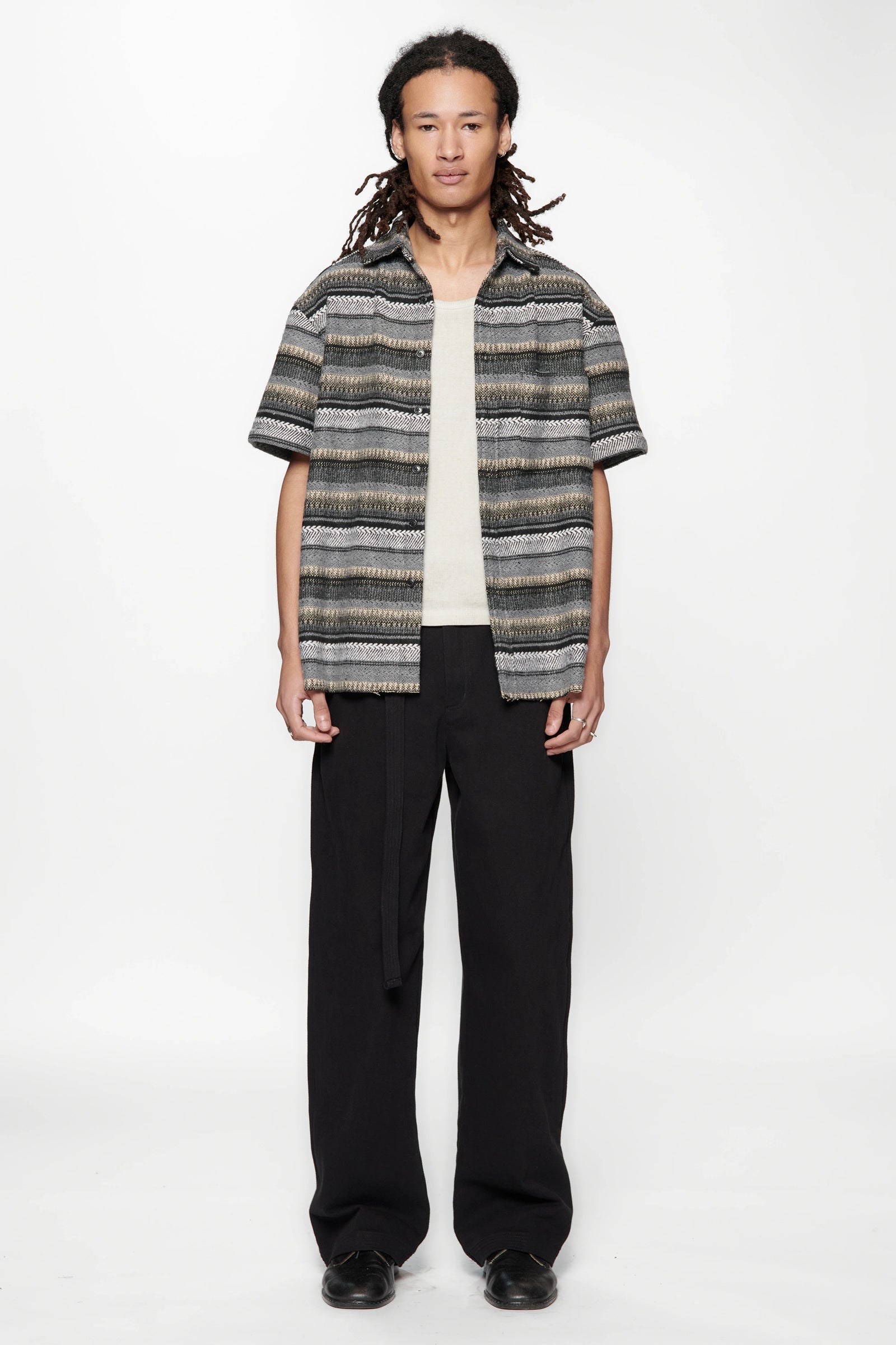 Person wearing a patterned shirt and black pants on a white background