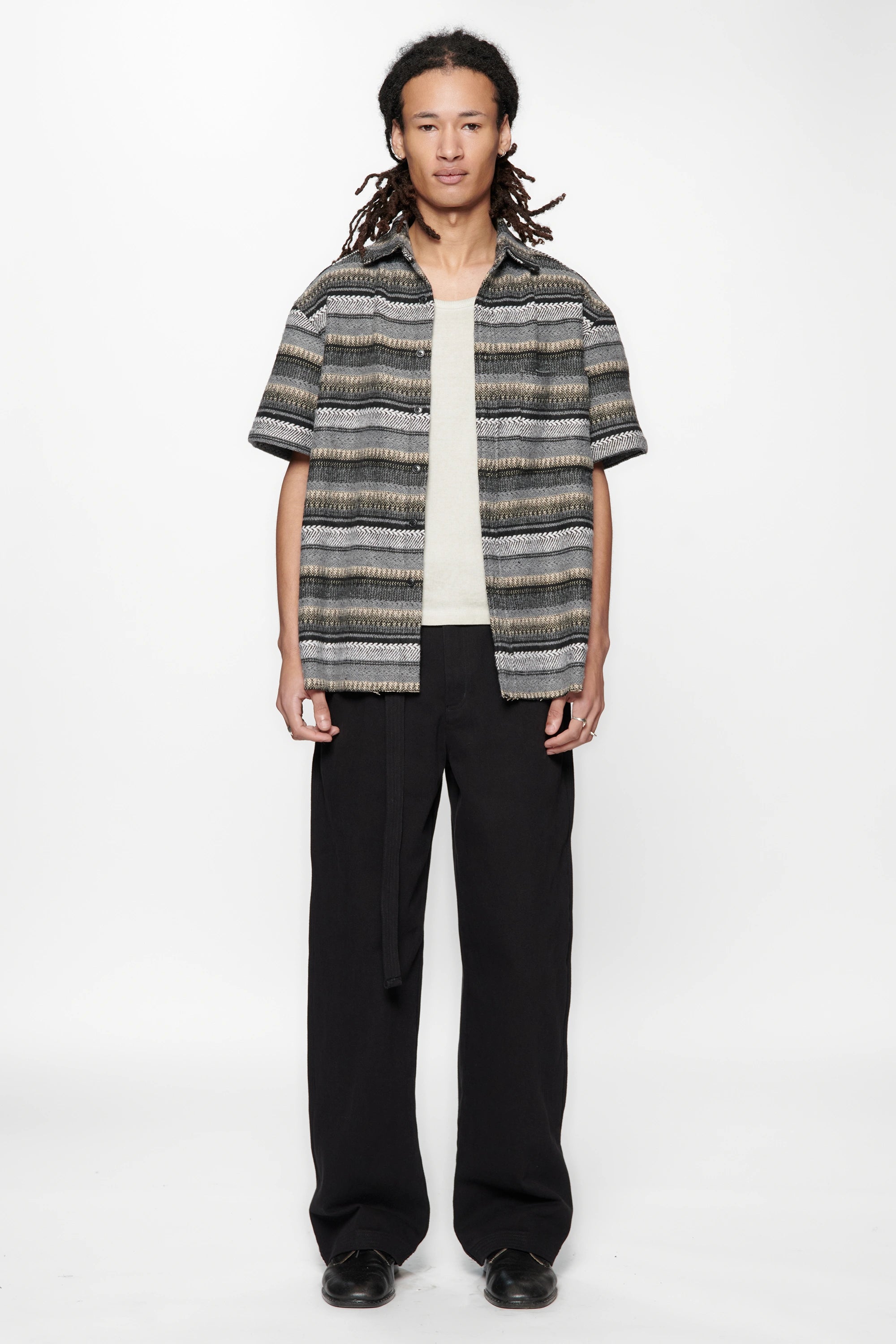 Person wearing a patterned shirt and black pants on a white background