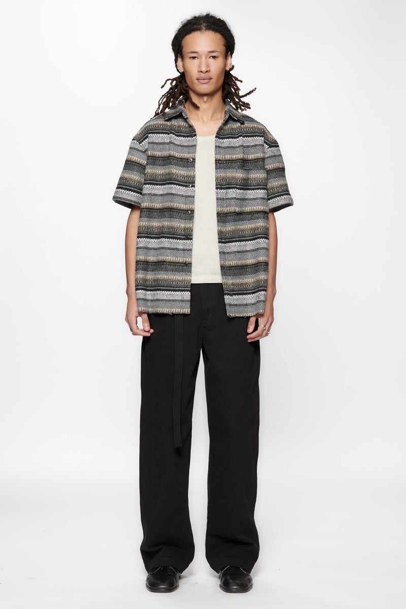 Person wearing a patterned shirt and black pants on a white background