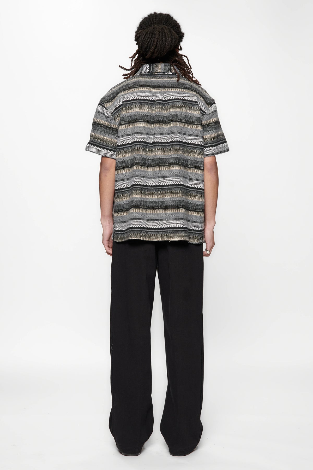 Person wearing a striped grey woven shirt and black pants on a white background