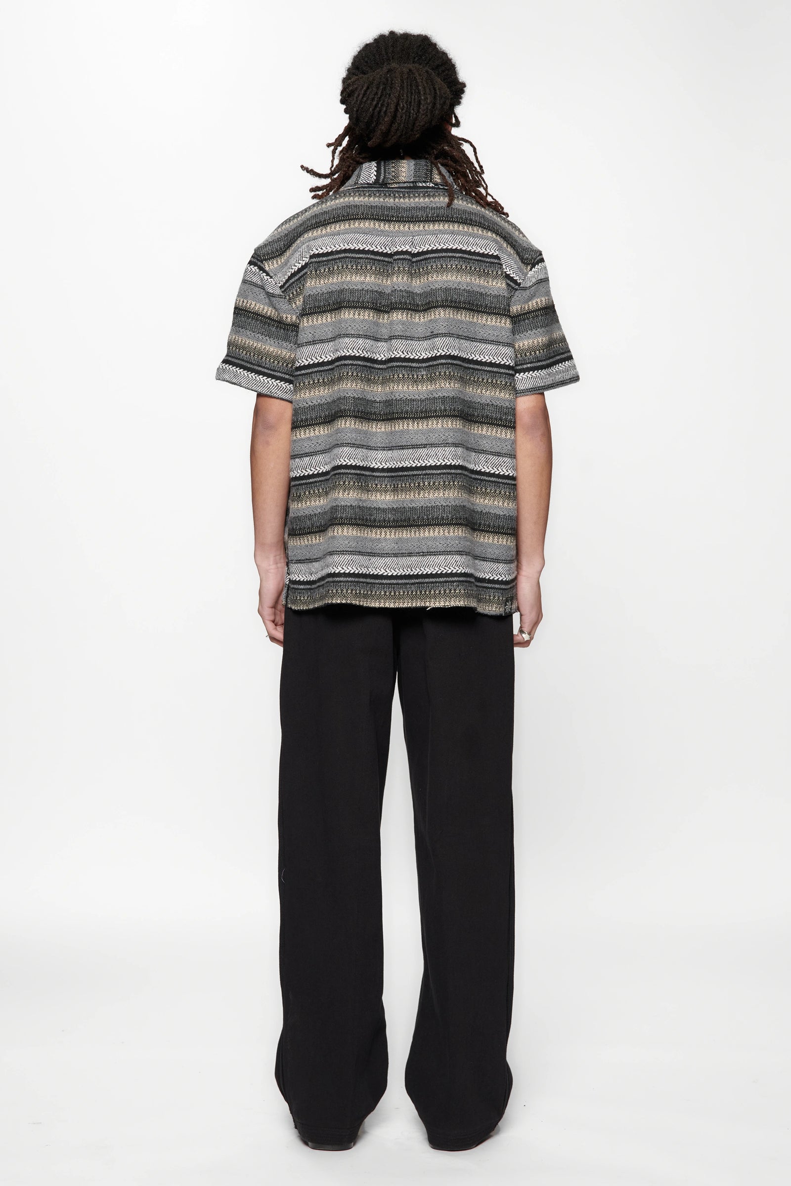 Person wearing a striped grey woven shirt and black pants on a white background