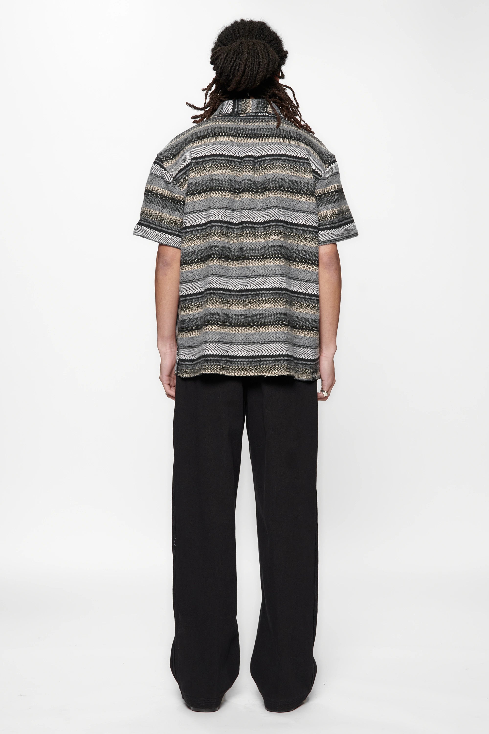Person wearing a striped grey woven shirt and black pants on a white background
