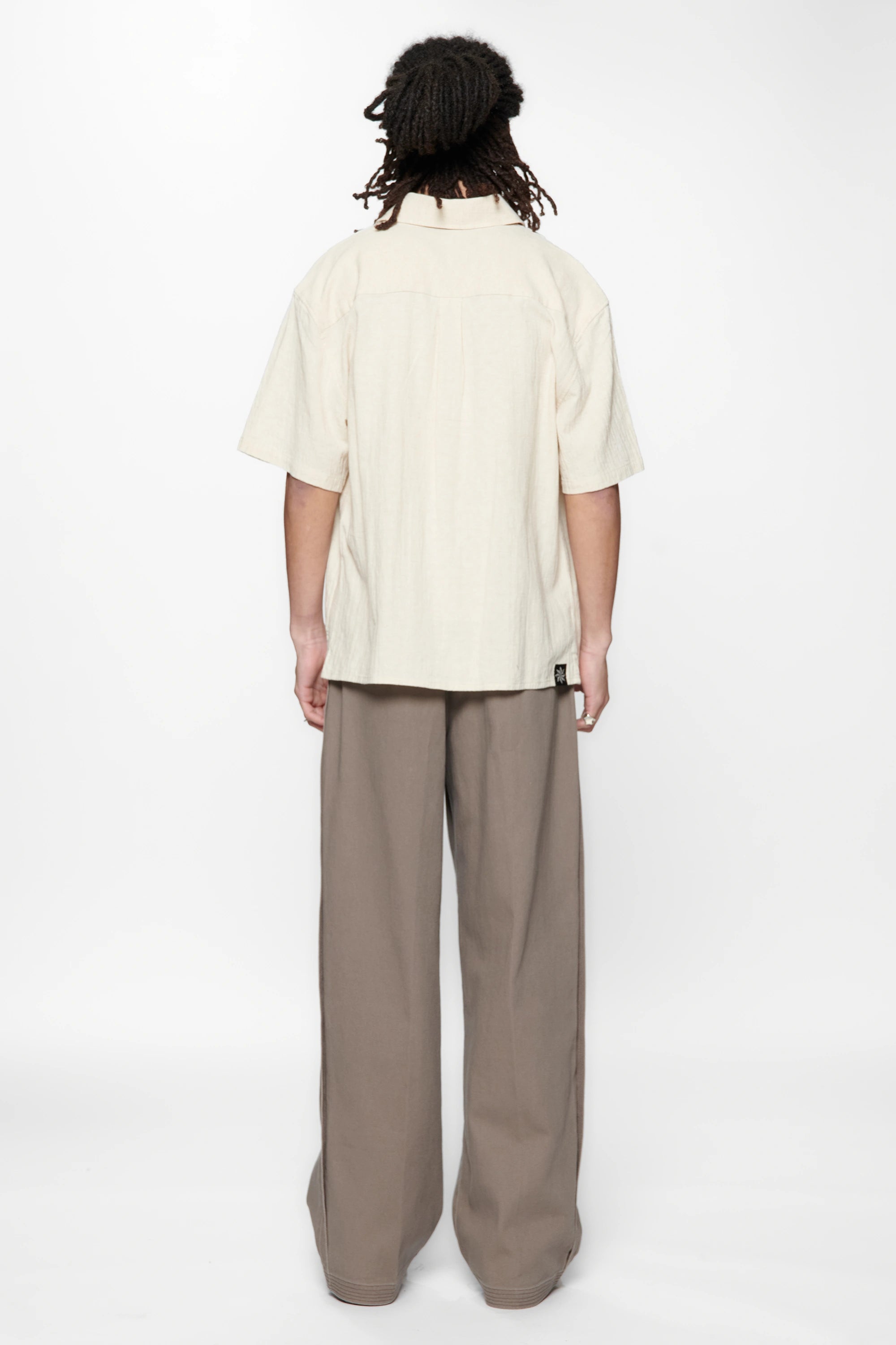 Behind view of a person wearing the Hold SS Shirt in Off White and brown pants