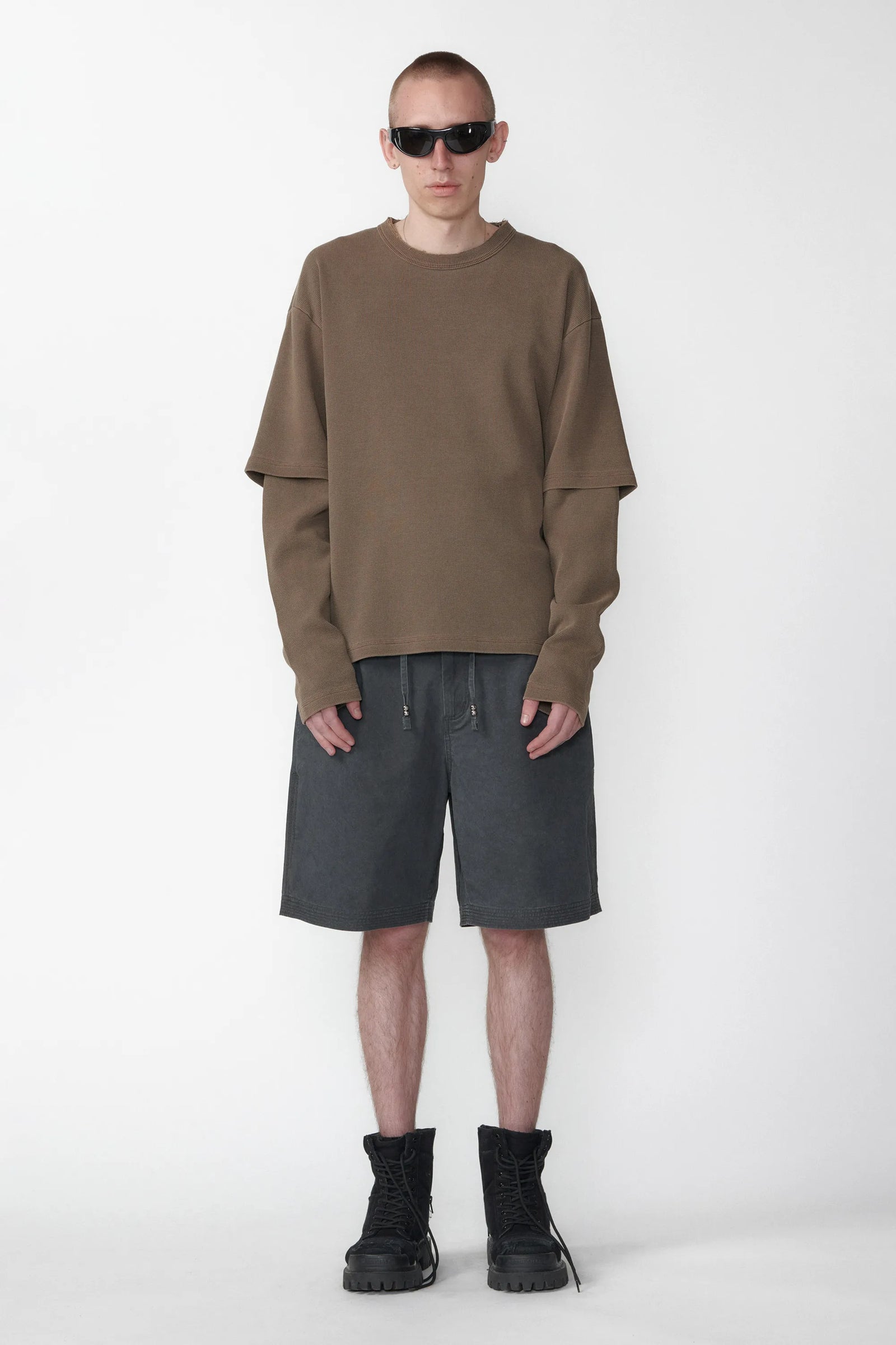 A person standing wearing relaxed fit charcoal grey shorts with an elastic waistband and a beige long-sleeve shirt