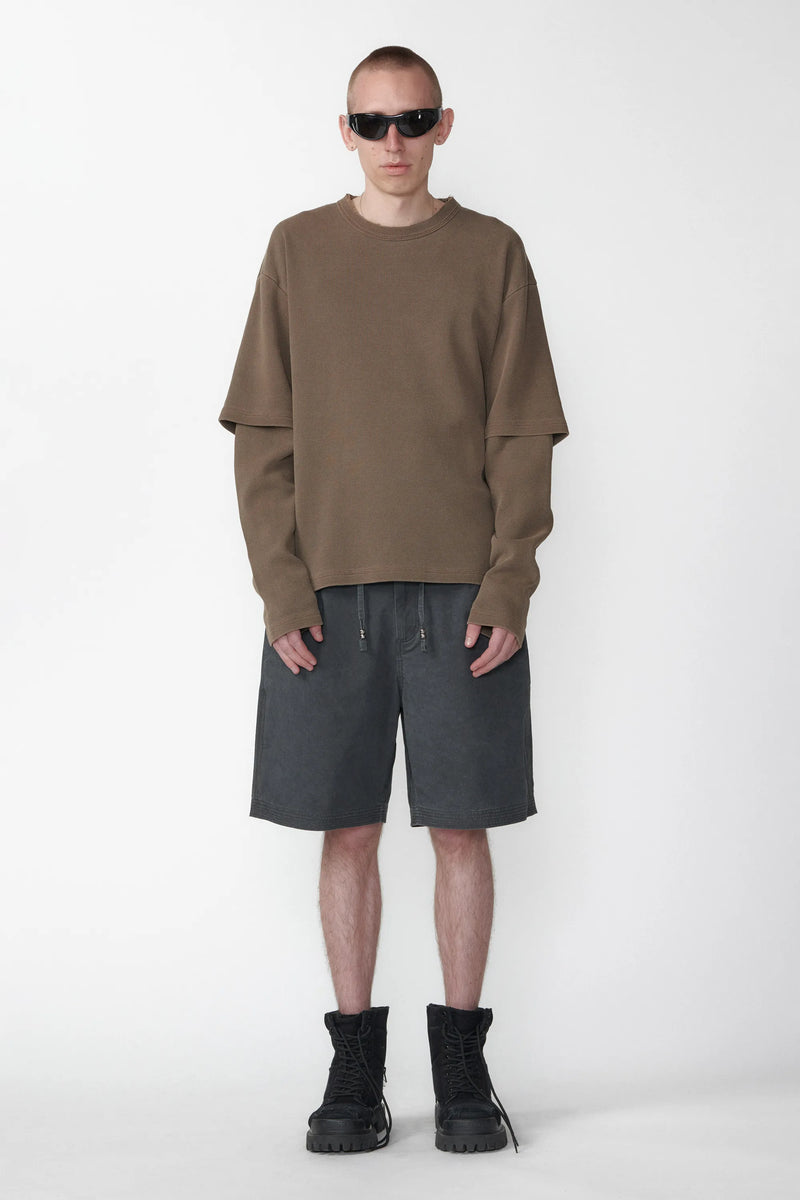 A person standing wearing relaxed fit charcoal grey shorts with an elastic waistband and a beige long-sleeve shirt